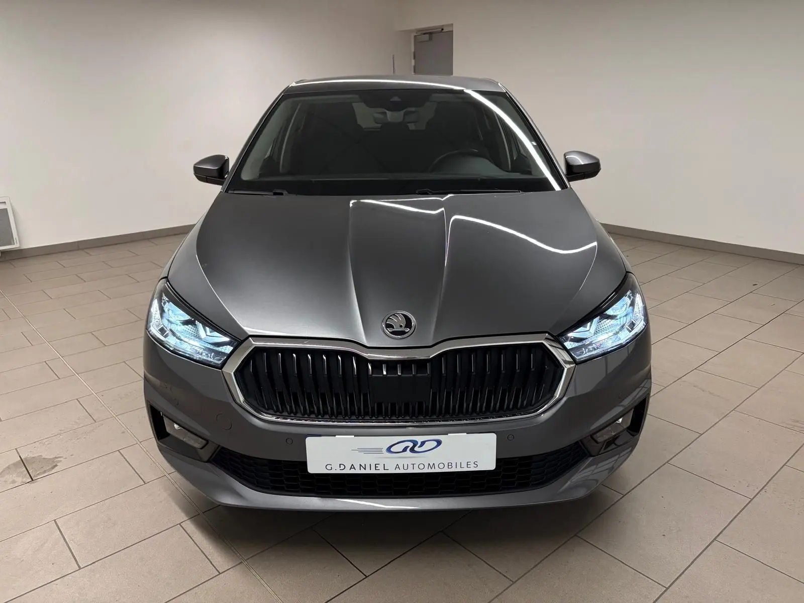 Vue avant d'une Skoda Fabia 2023 gris graphite métallisé avec phares allumés dans un showroom.