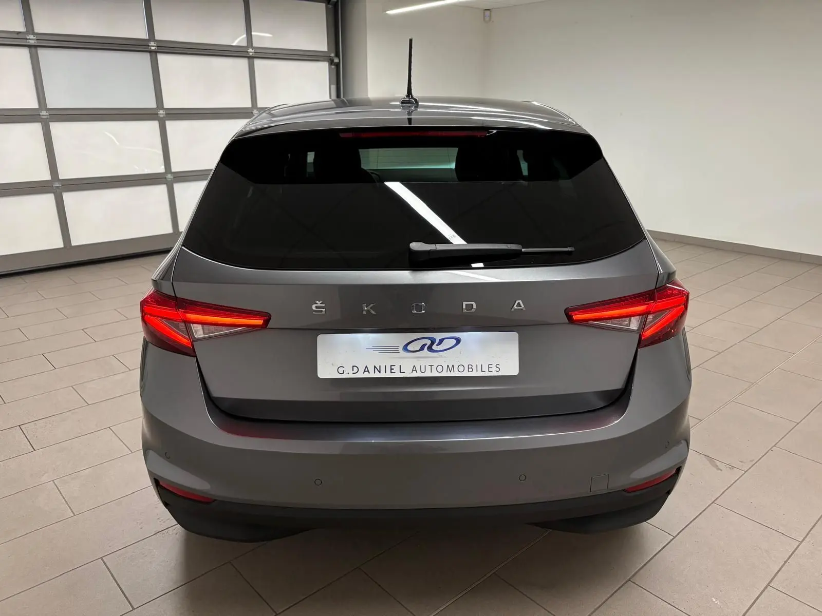 Vue arrière d'une Skoda Fabia 2023 gris graphite métallisé avec feux arrière allumés dans un garage.