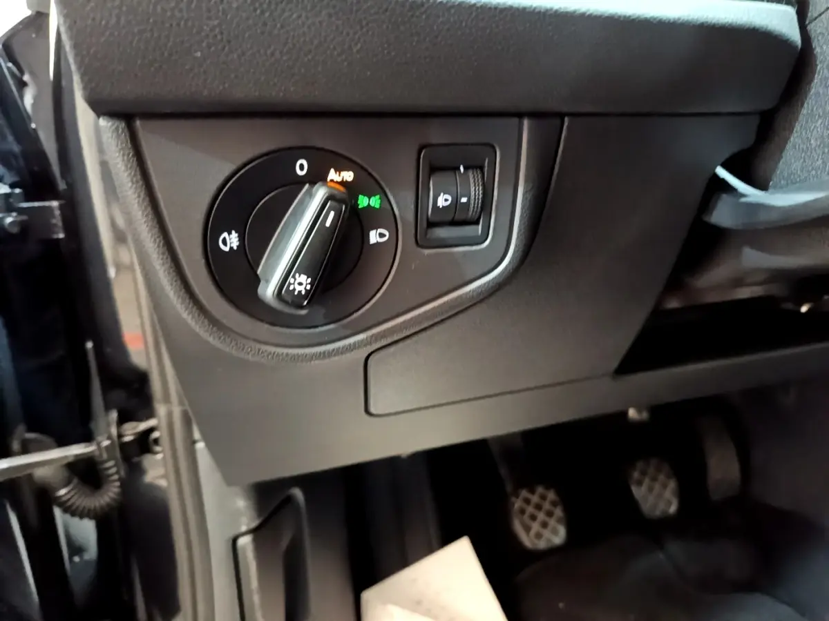 Gros plan sur le bouton de réglage des phares à gauche du tableau de bord d’un Volkswagen Taigo noir 2023.