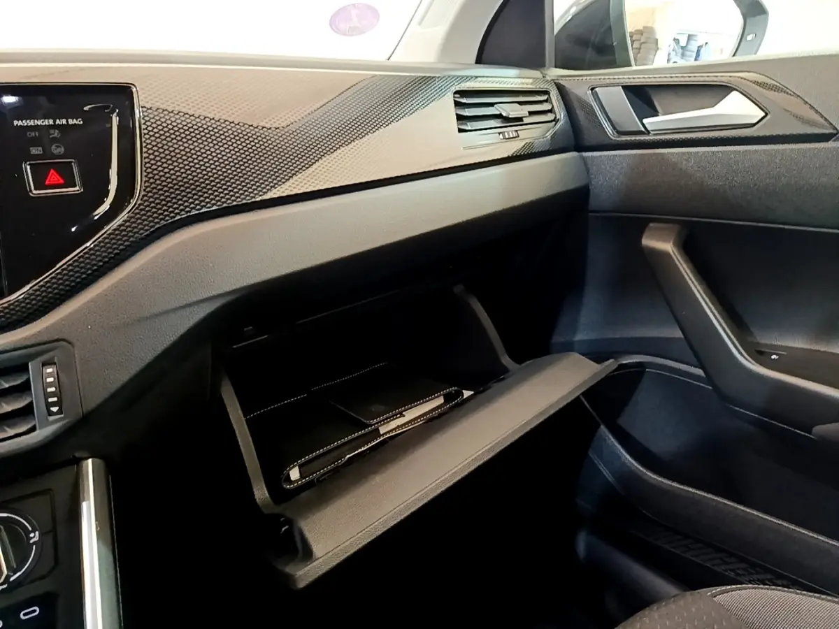 Intérieur côté passager du Volkswagen Taigo noir 2023, boîte à gants ouverte avec carnet à l'intérieur.