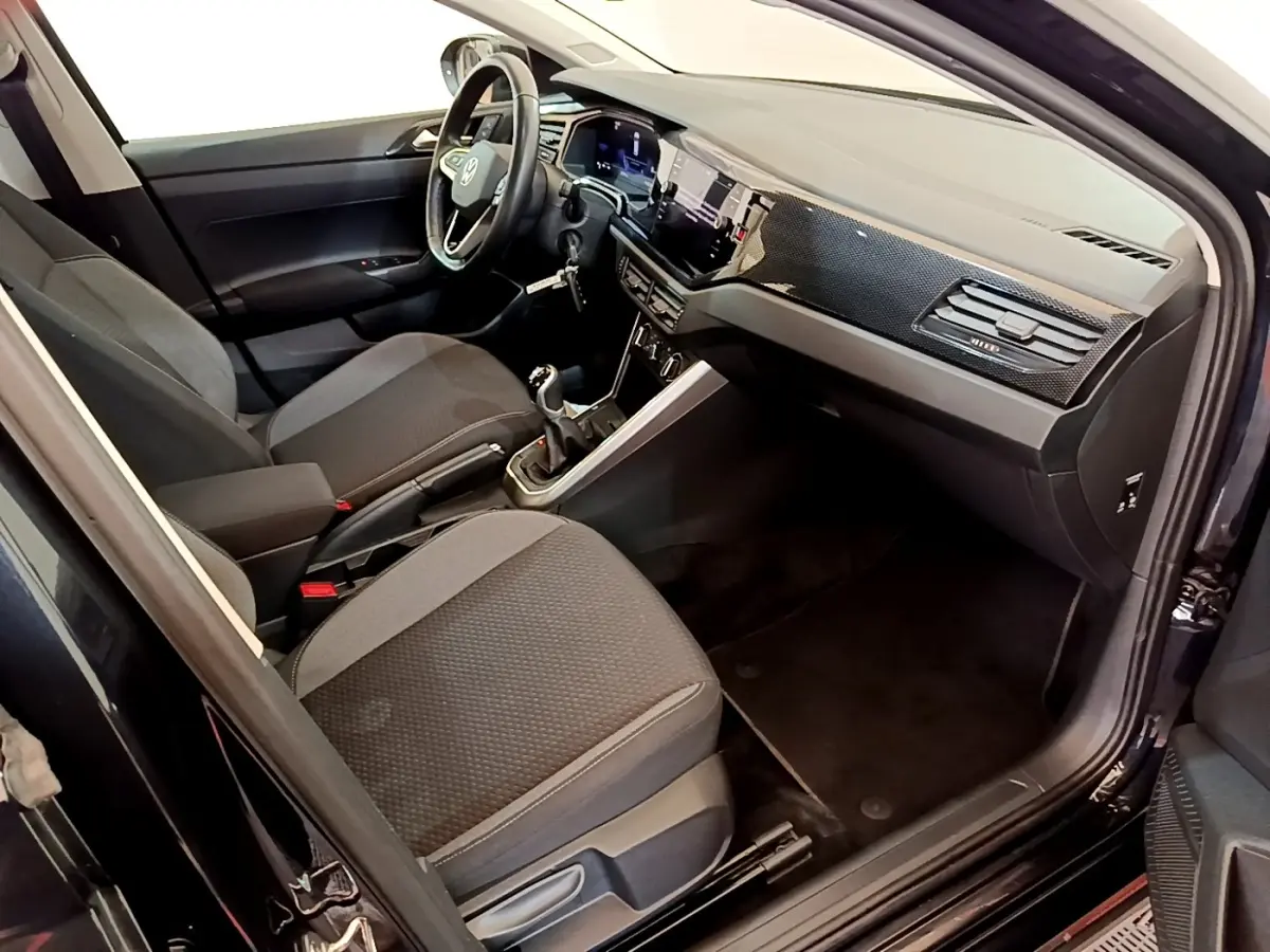 Intérieur avant droit du Volkswagen Taigo noir 2023, avec tableau de bord moderne et boîte manuelle visible.