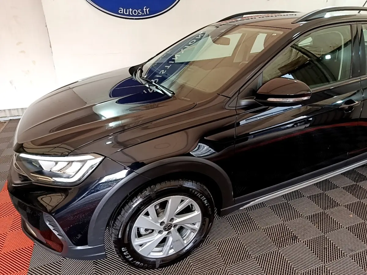 Volkswagen Taigo noir en 3/4 avant droit, avec phares LED et jantes alliage visibles en intérieur showroom.