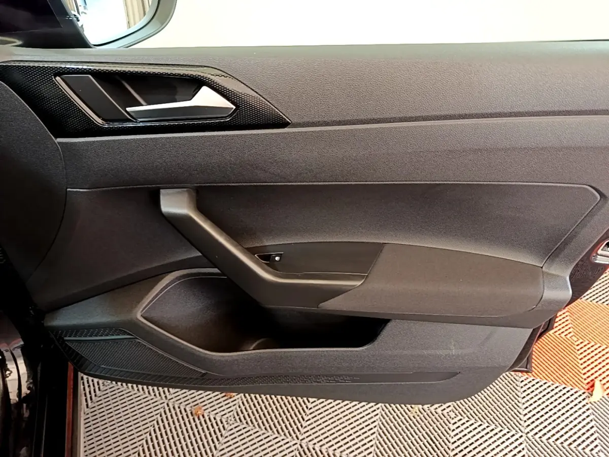 Vue rapprochée de la porte intérieure côté conducteur du Volkswagen Taigo noir, avec poignée et panneau de commande des vitres.