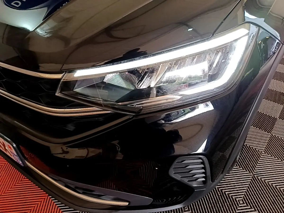 Gros plan sur le phare avant droit allumé d'un Volkswagen Taigo noir 2023, mettant en valeur la calandre et les détails LED.