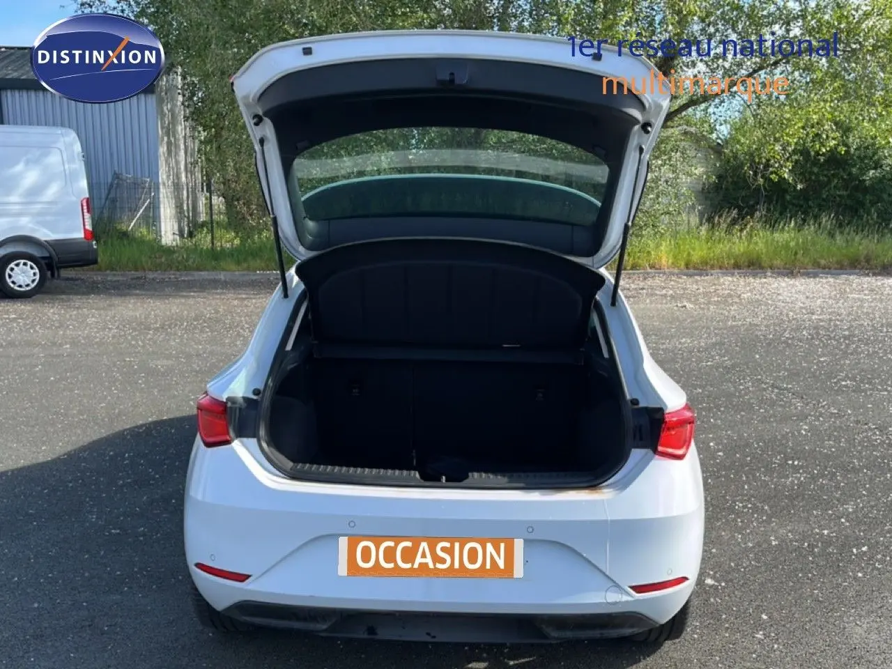 Vue arrière d'une SEAT Leon blanc neige 2025 avec coffre ouvert sur un parking extérieur.