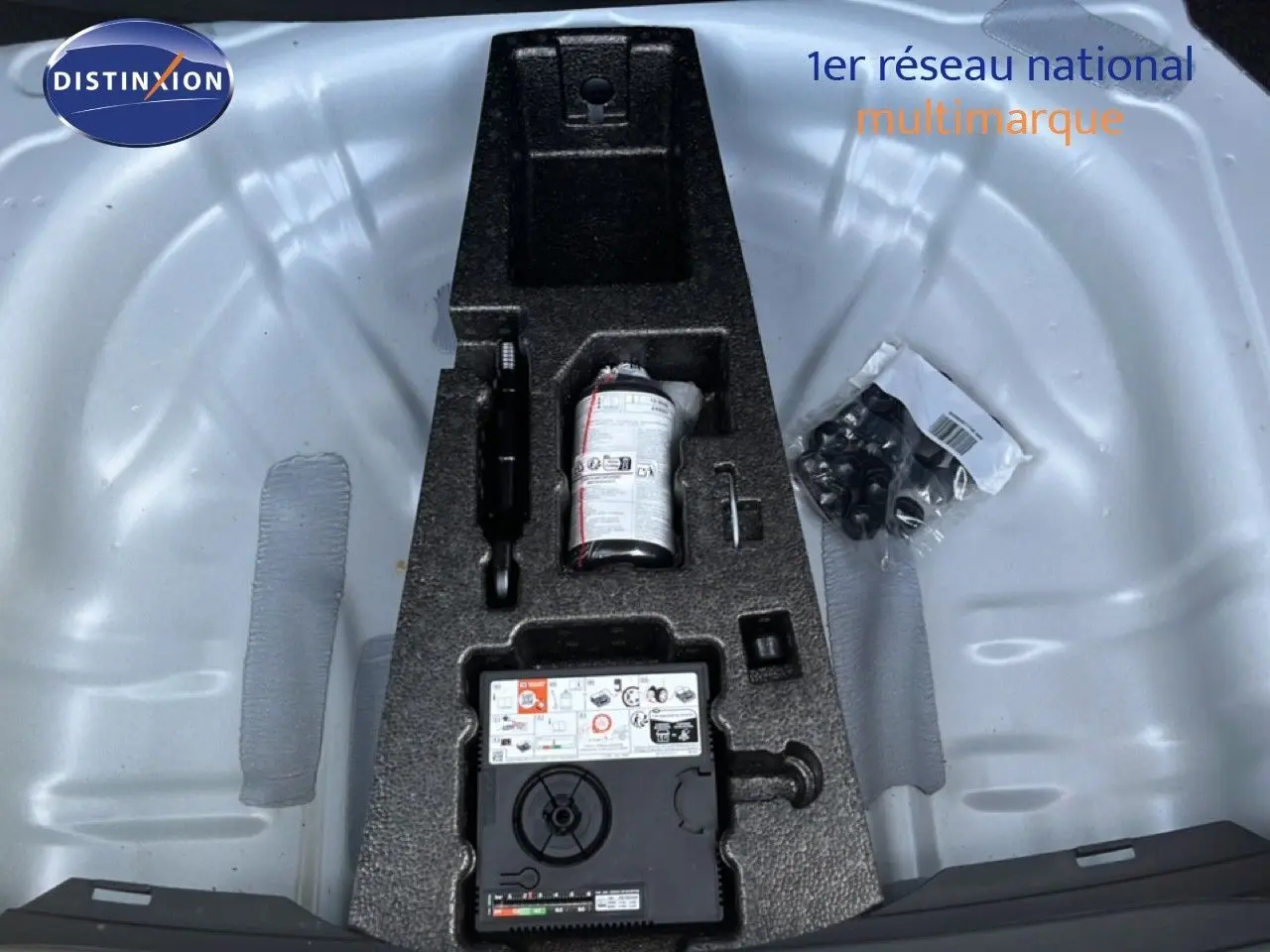 Vue plongeante sur le coffre ouvert d'une SEAT LEON blanc neige, montrant le rangement d'outils et kit de réparation.