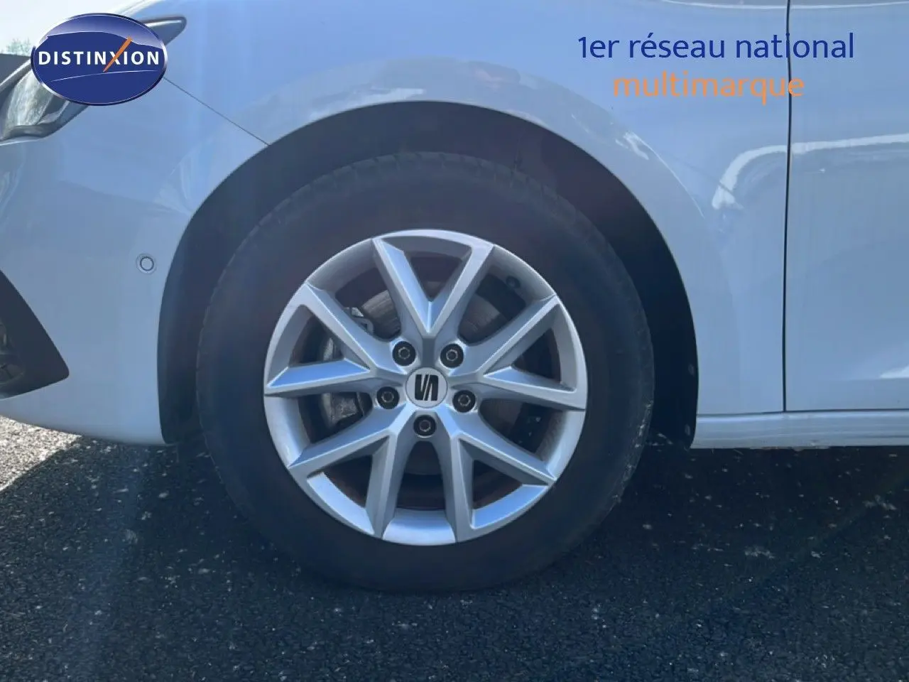 Gros plan sur la roue avant gauche d'une SEAT Leon blanc neige, mettant en valeur la jante en alliage argentée.