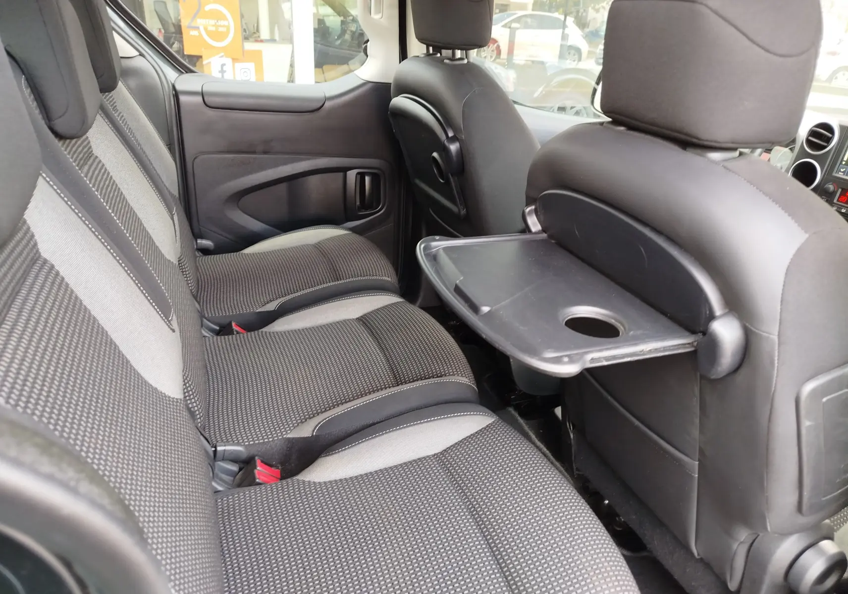 Vue intérieure côté droit du Peugeot Partner Tepee gris foncé, montrant les sièges arrière en tissu et une tablette rabattable.