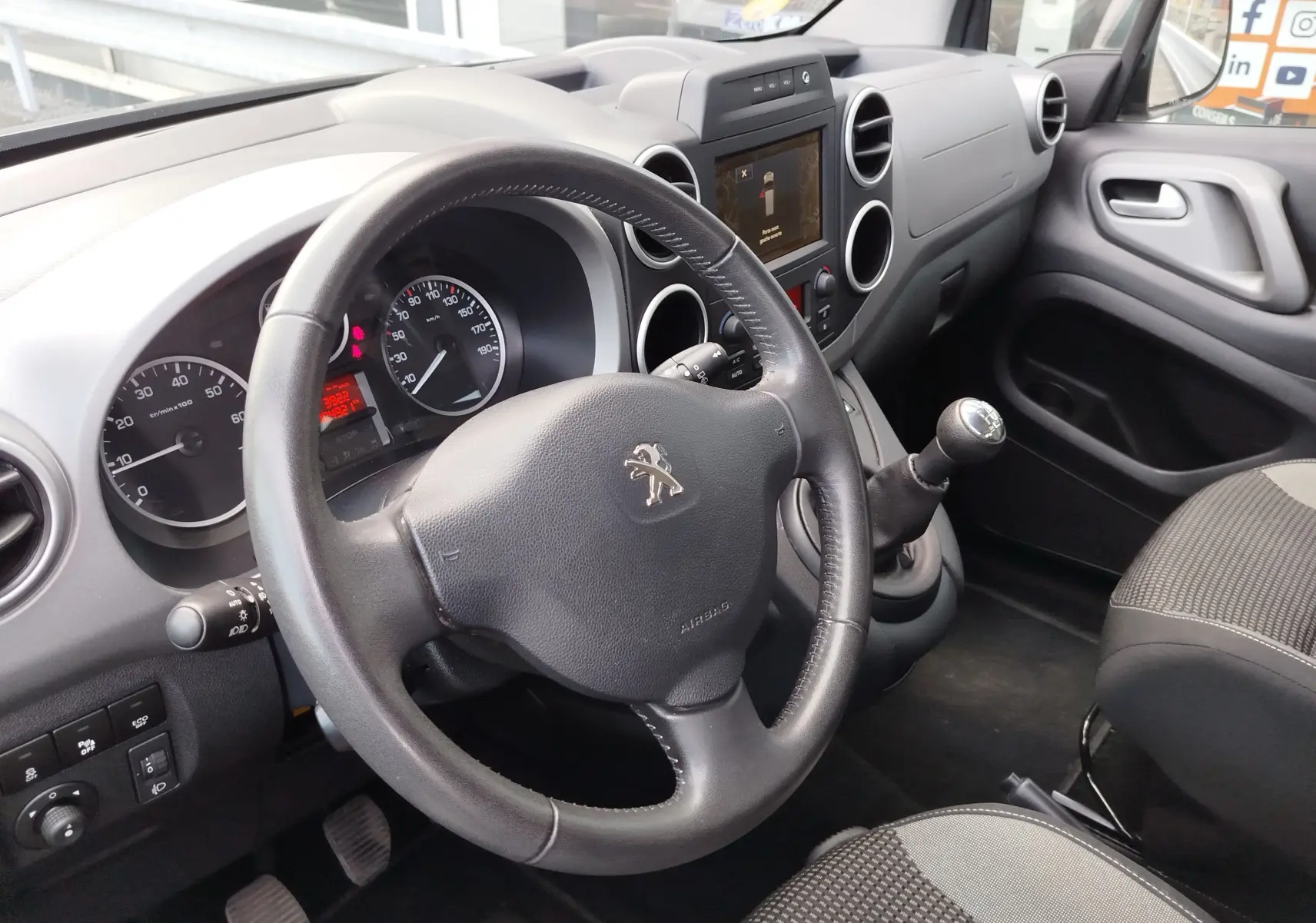 Vue intérieure côté conducteur du Peugeot Partner Tepee 2017, volant cuir, levier de vitesse manuel et tableau de bord gris.