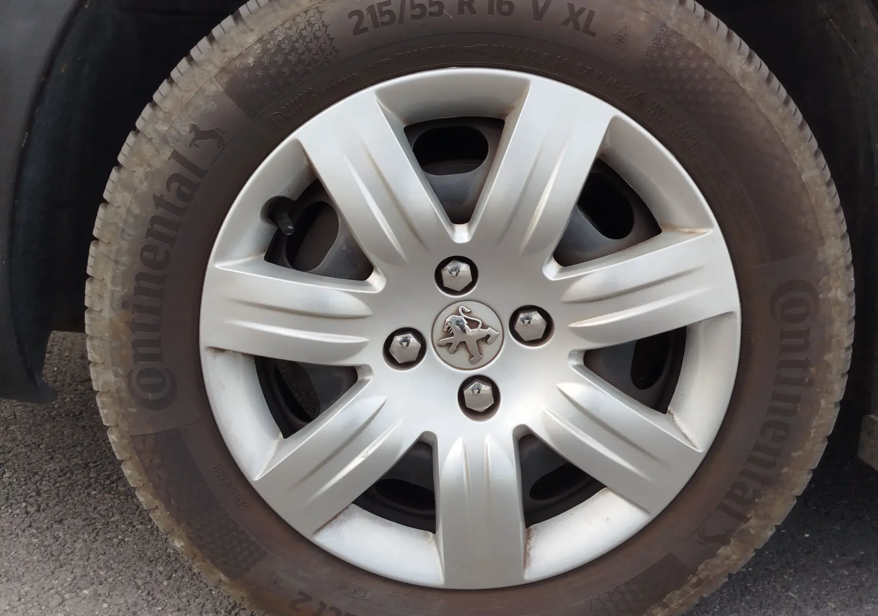 Gros plan sur la roue avant droite d’un Peugeot Partner Tepee gris foncé avec jante en alliage et logo lion au centre.