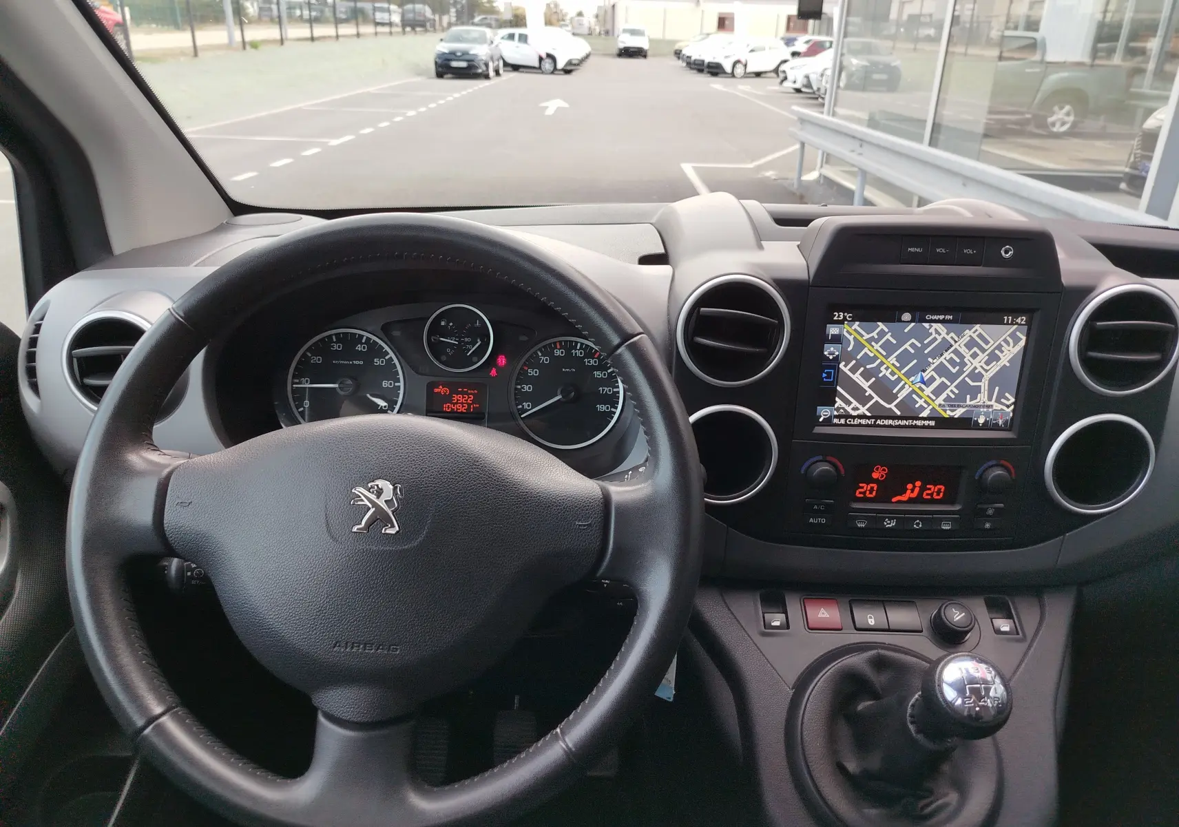 Vue intérieure du tableau de bord du Peugeot Partner Tepee gris foncé, avec volant, écran GPS et levier de vitesses manuel.