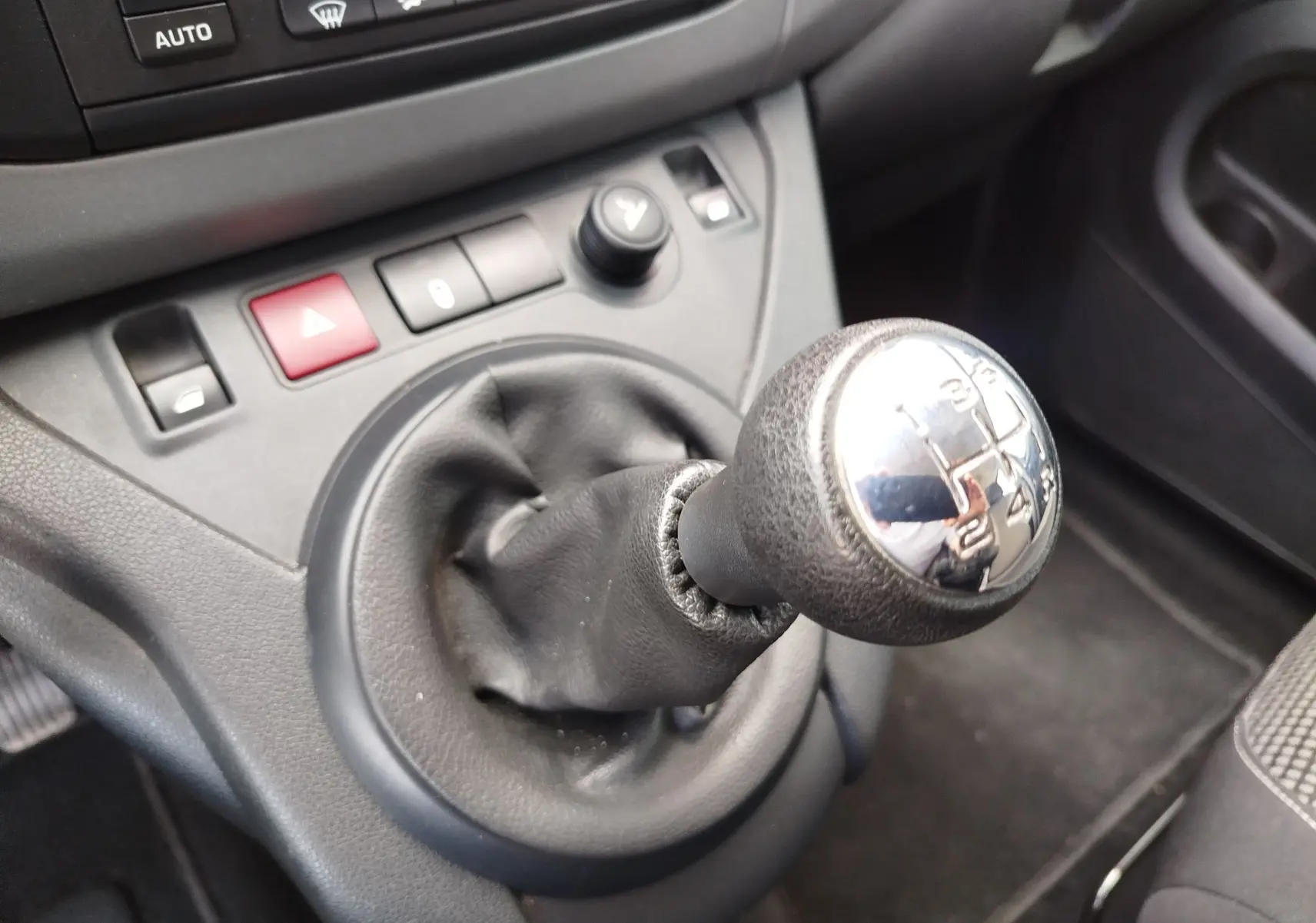 Gros plan sur le levier de vitesse manuel noir du Peugeot Partner Tepee gris foncé, avec boutons de commande proches.