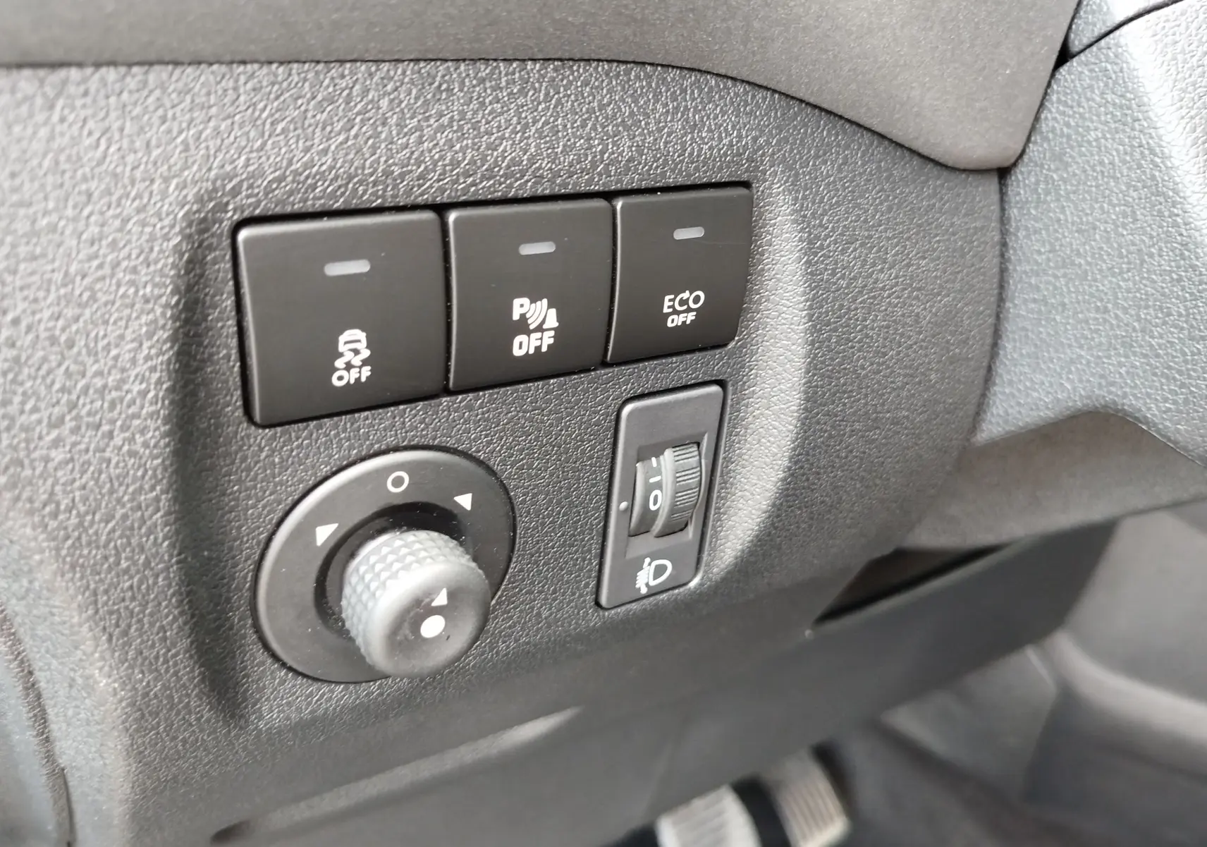 Gros plan sur les commandes de réglage des phares et des aides à la conduite dans un Peugeot Partner Tepee gris foncé, intérieur noir.