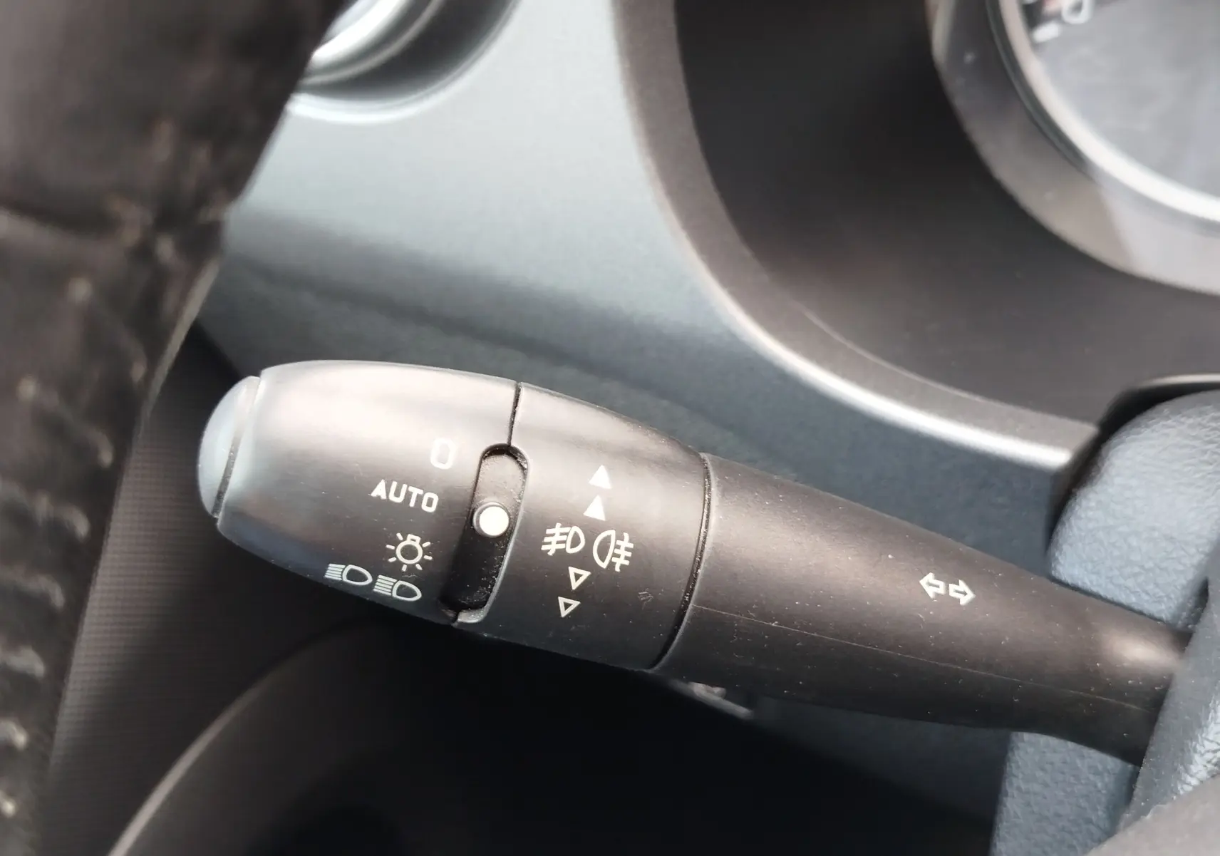 Gros plan sur la manette de commandes des phares et clignotants à gauche du volant dans un Peugeot Partner Tepee gris foncé 2017.