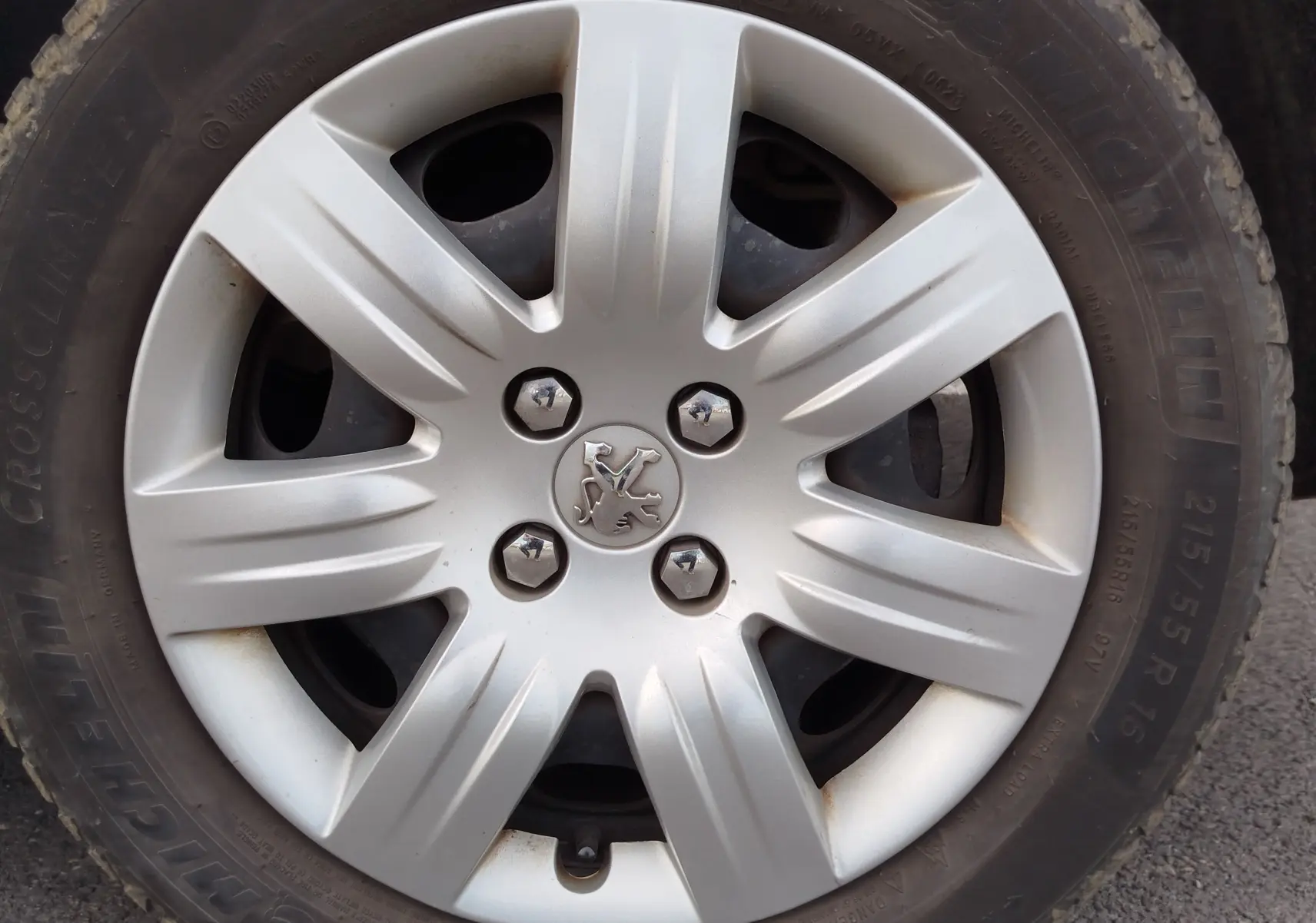 Gros plan sur la jante argentée avec logo Peugeot au centre, montée sur pneu Michelin d’un Partner Tepee gris foncé.