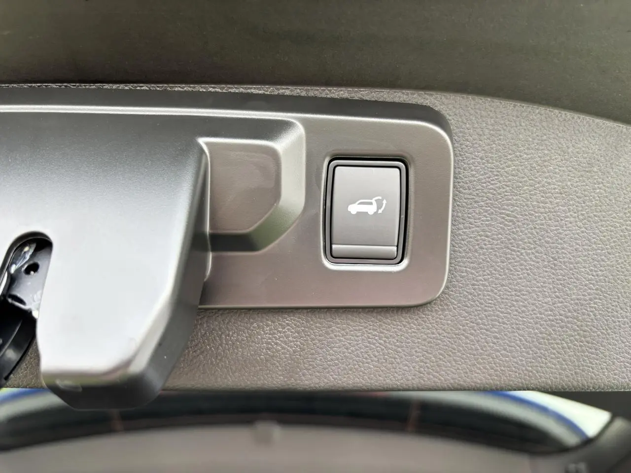 Gros plan sur le bouton d'ouverture mains-libres du hayon du Renault Austral bleu Iron Metal, intérieur du coffre visible.