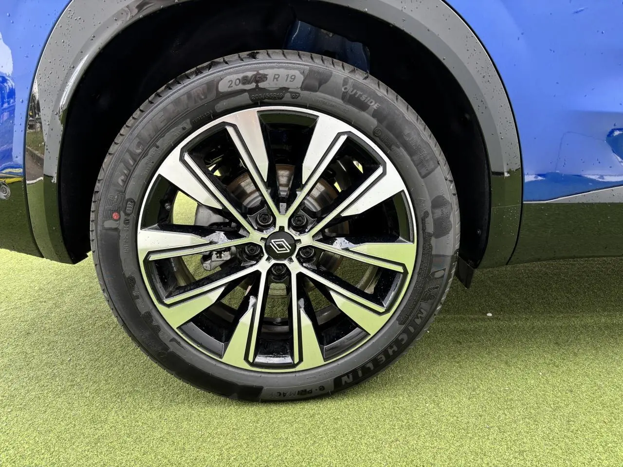 Gros plan sur la jante alliage 19 pouces Komah diamantée noire du côté gauche du Renault Austral bleu Iron Metal.