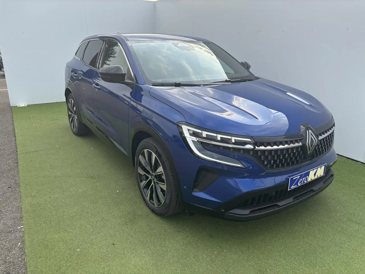 Renault Austral bleu Iron Metal en 3/4 avant droit, avec calandre damier ice black et jantes alliage noires.