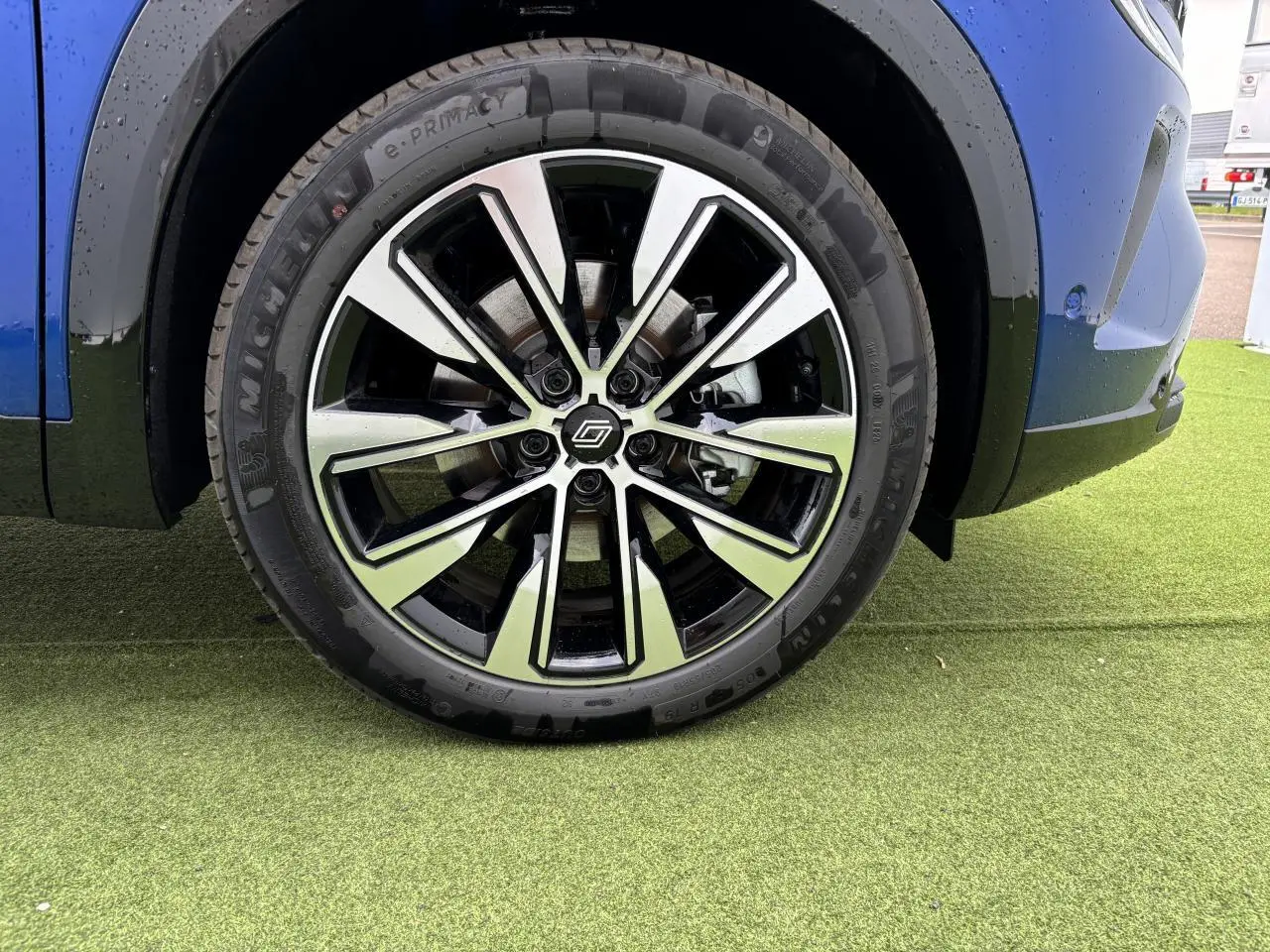 Gros plan sur la jante alliage 19 pouces Komah diamantée noire du côté avant droit du Renault Austral bleu Iron Metal.