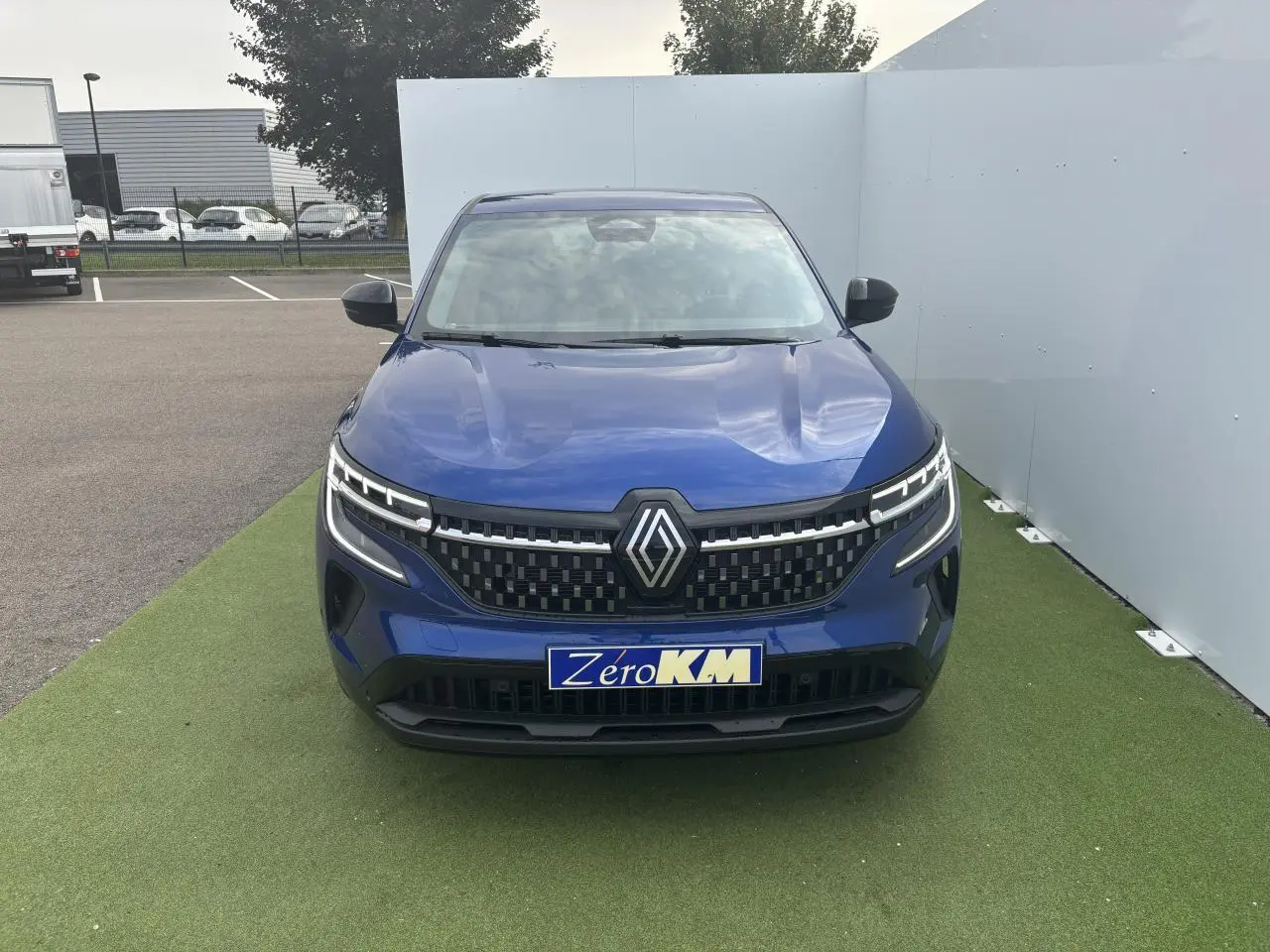 Vue frontale d'un Renault Austral bleu Iron Metal avec calandre à damier et feux LED distinctifs allumés.