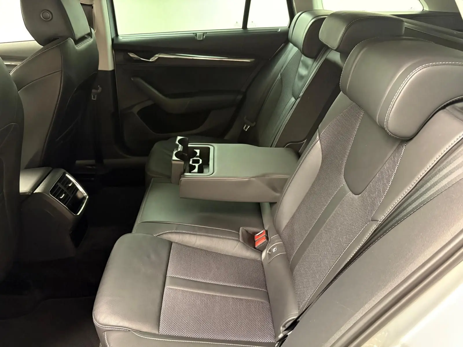 Vue intérieure côté droit des sièges arrière en cuir noir avec accoudoir central déployé de la Skoda Octavia Combi 2023 gris argent.