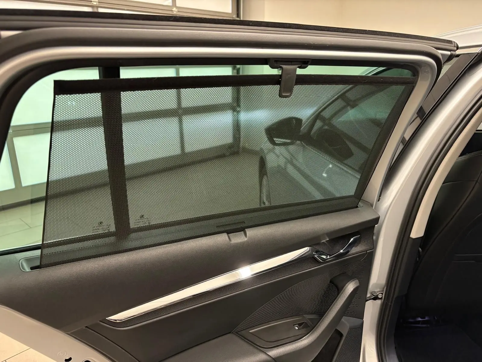 Vue intérieure de la porte arrière droite d'une Skoda Octavia Combi gris argent 2023 avec pare-soleil en filet déployé.