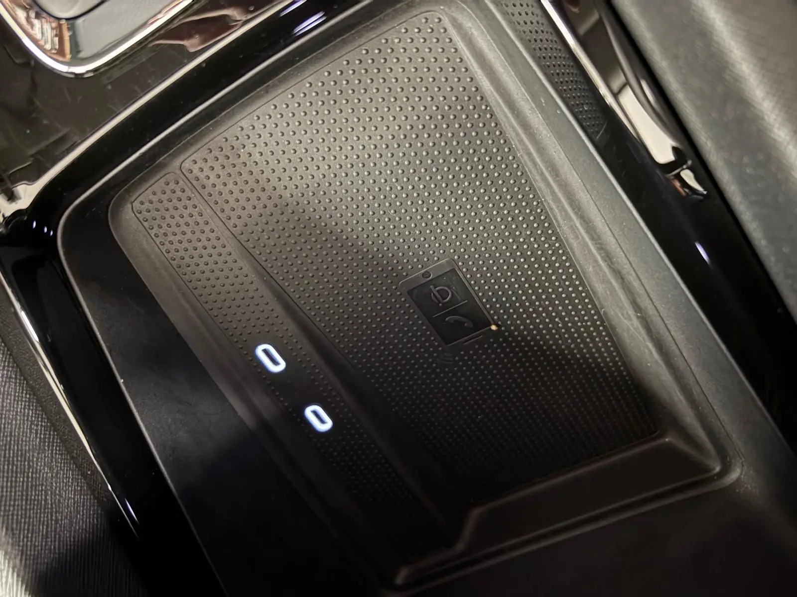 Gros plan sur le chargeur sans fil noir avec indicateurs lumineux dans le compartiment central d'une Skoda Octavia Combi gris argent 2023.