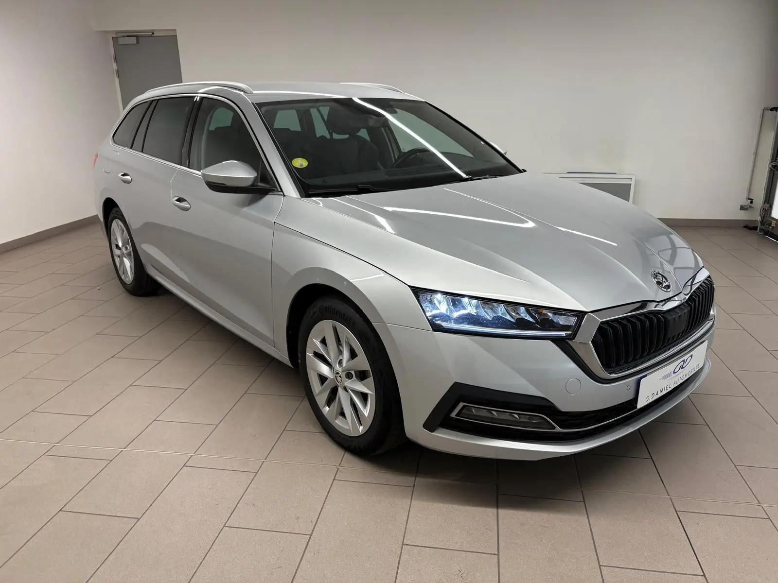 Skoda Octavia Combi gris argent vue 3/4 avant droit, phares LED allumés et calandre noire distinctive.