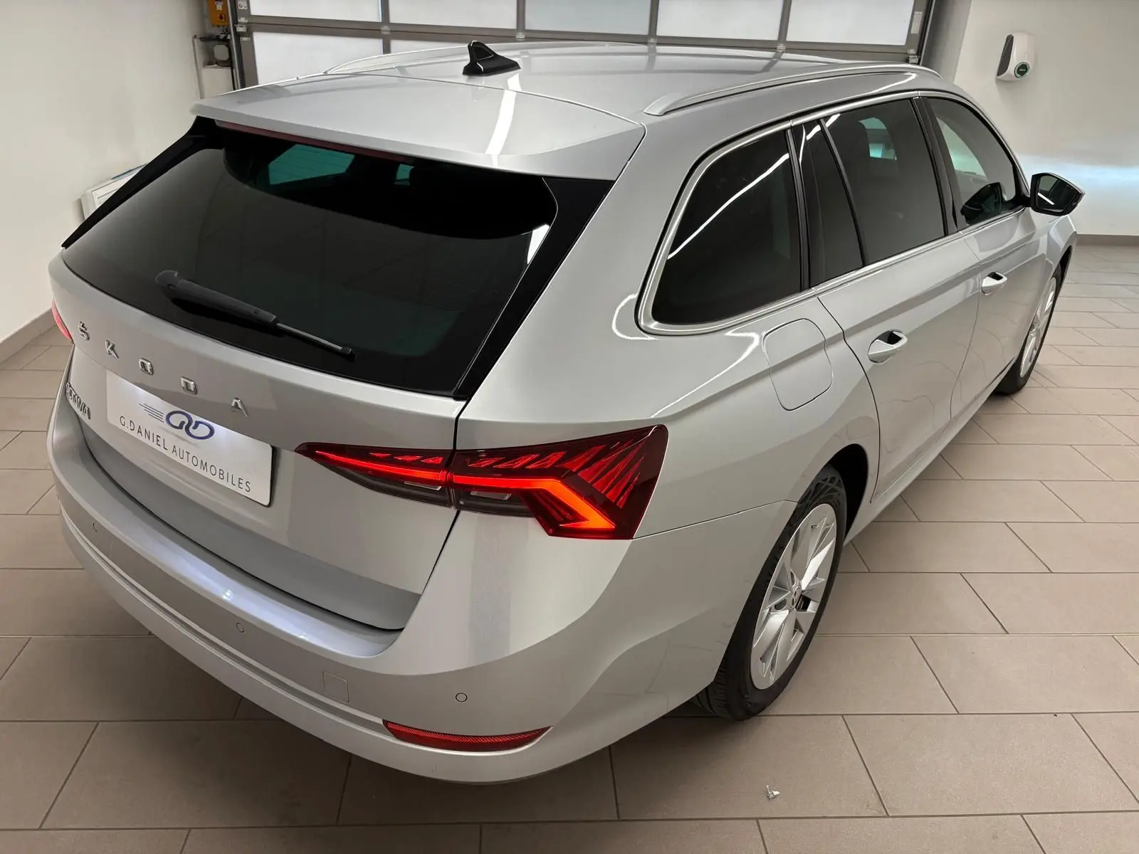 Vue 3/4 arrière droite d'une Skoda Octavia Combi gris argent 2023 avec feux arrière LED allumés dans un garage.