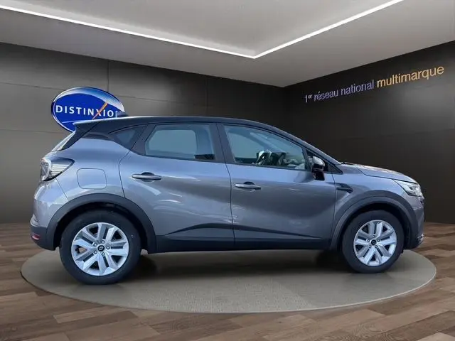 Profil droit du Renault Captur 2024 gris Cassiopée avec toit noir et jantes 17 pouces en intérieur showroom.