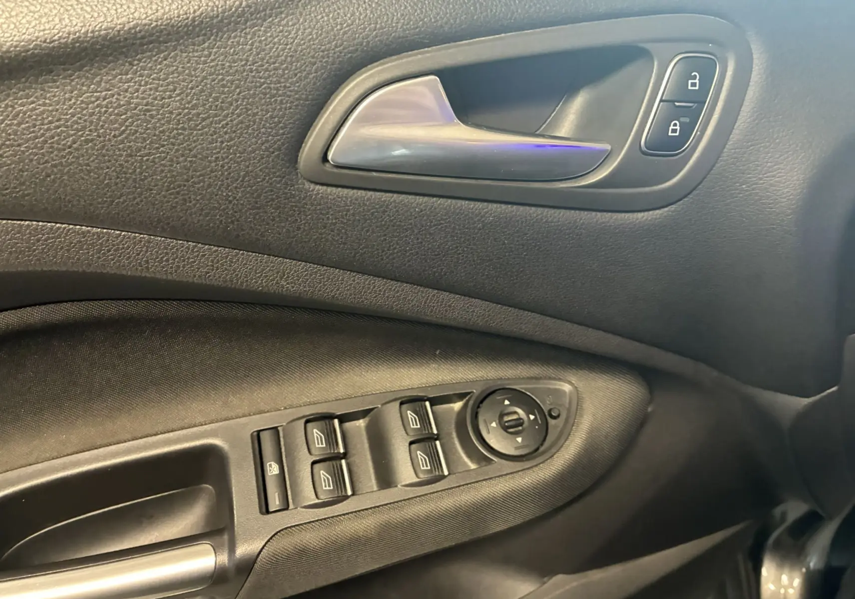 Gros plan sur la porte côté conducteur du Ford C-MAX gris, montrant la poignée intérieure et les commandes des vitres électriques.