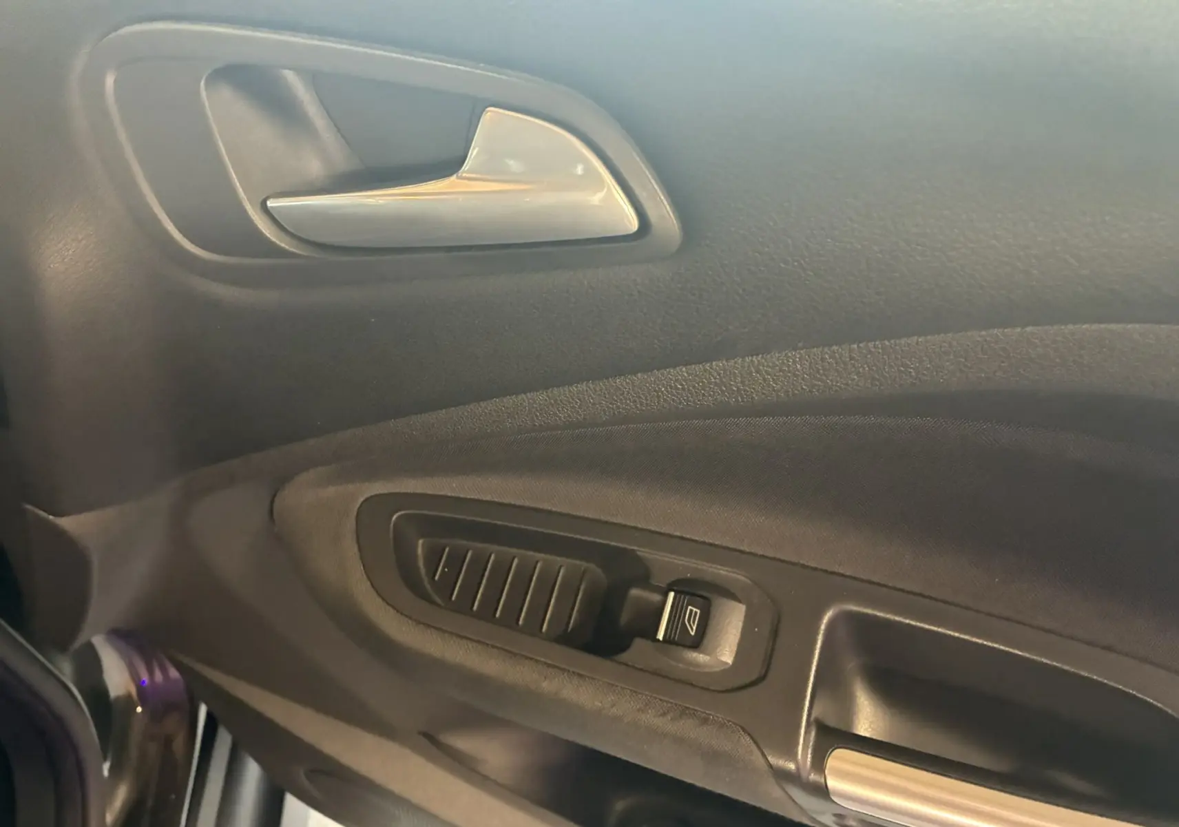 Gros plan sur la poignée intérieure et le bouton de lève-vitre côté gauche d'une Ford C-MAX gris foncé de 2015.