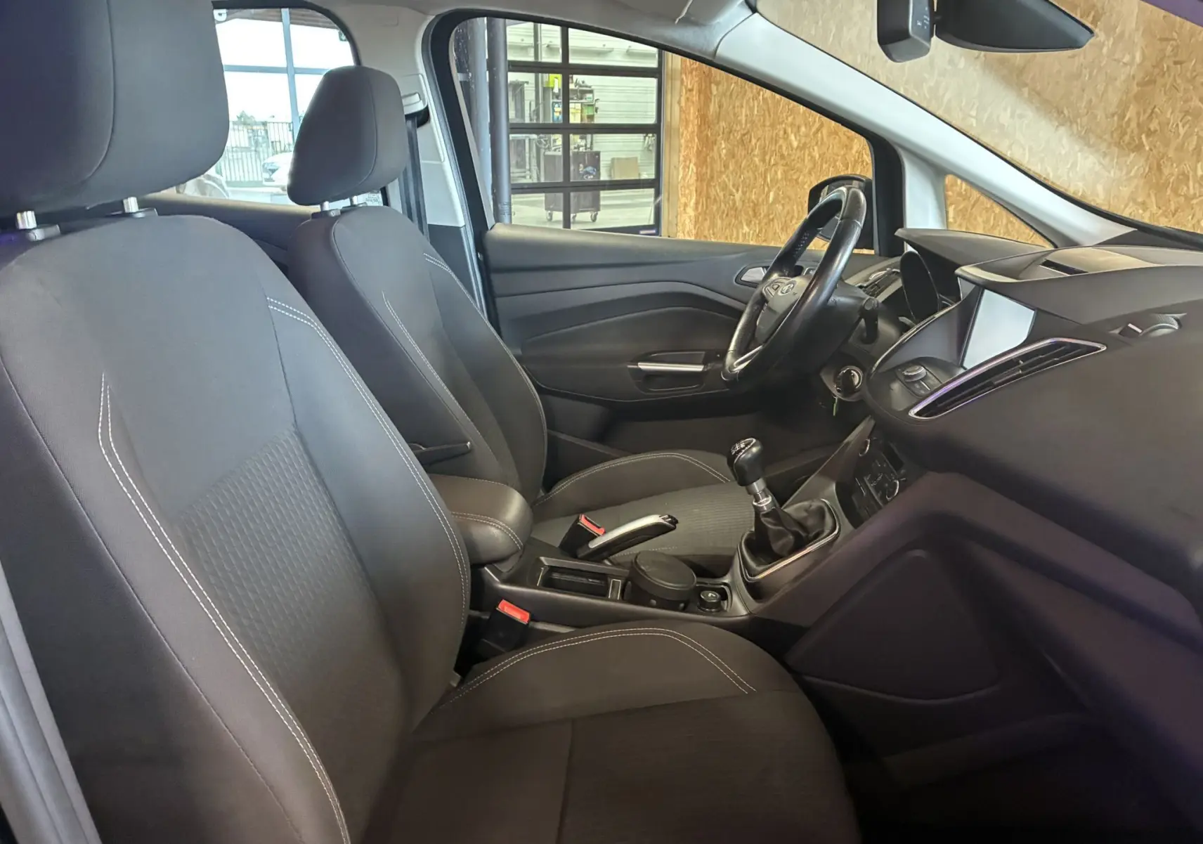 Intérieur avant droit d'une Ford C-MAX gris 2015, montrant sièges tissu gris noir et tableau de bord avec boîte manuelle.