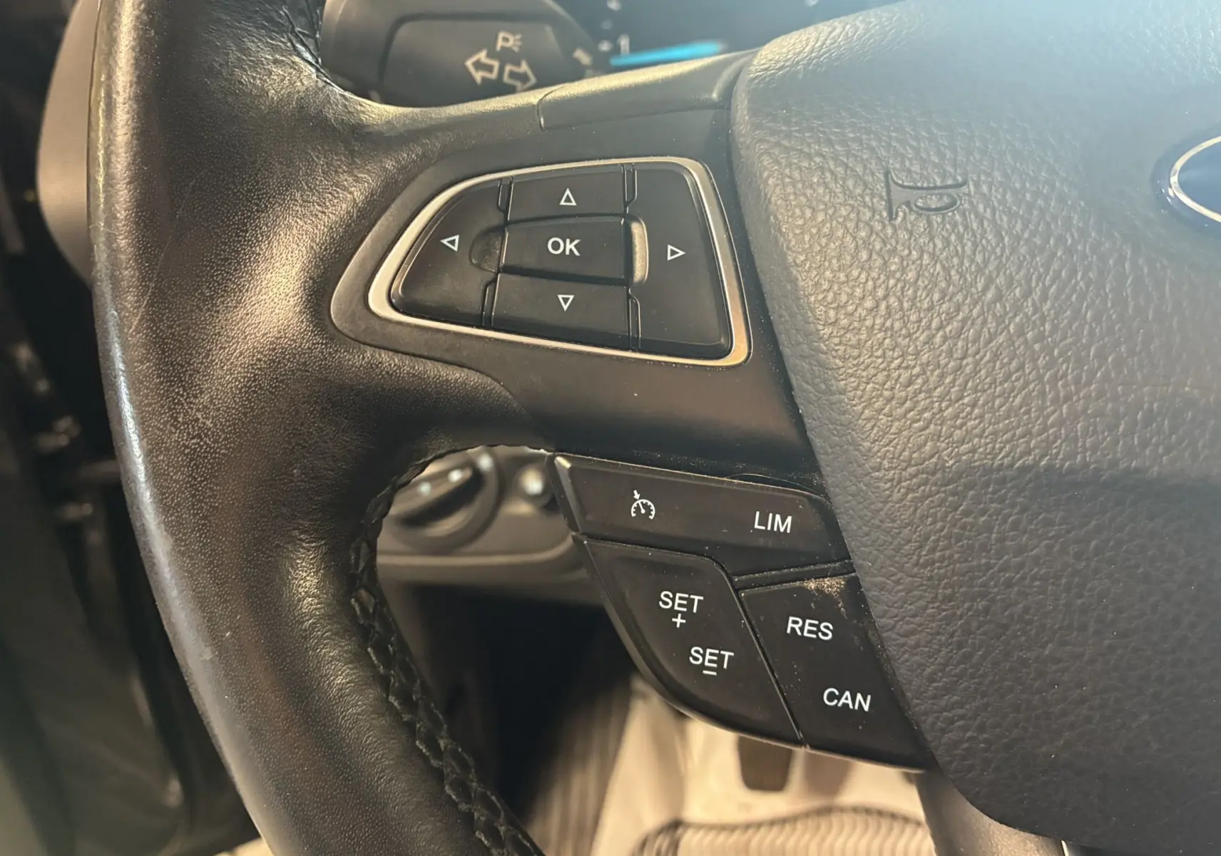 Gros plan sur le volant noir en cuir du Ford C-MAX gris, montrant les commandes de régulateur de vitesse et de navigation.