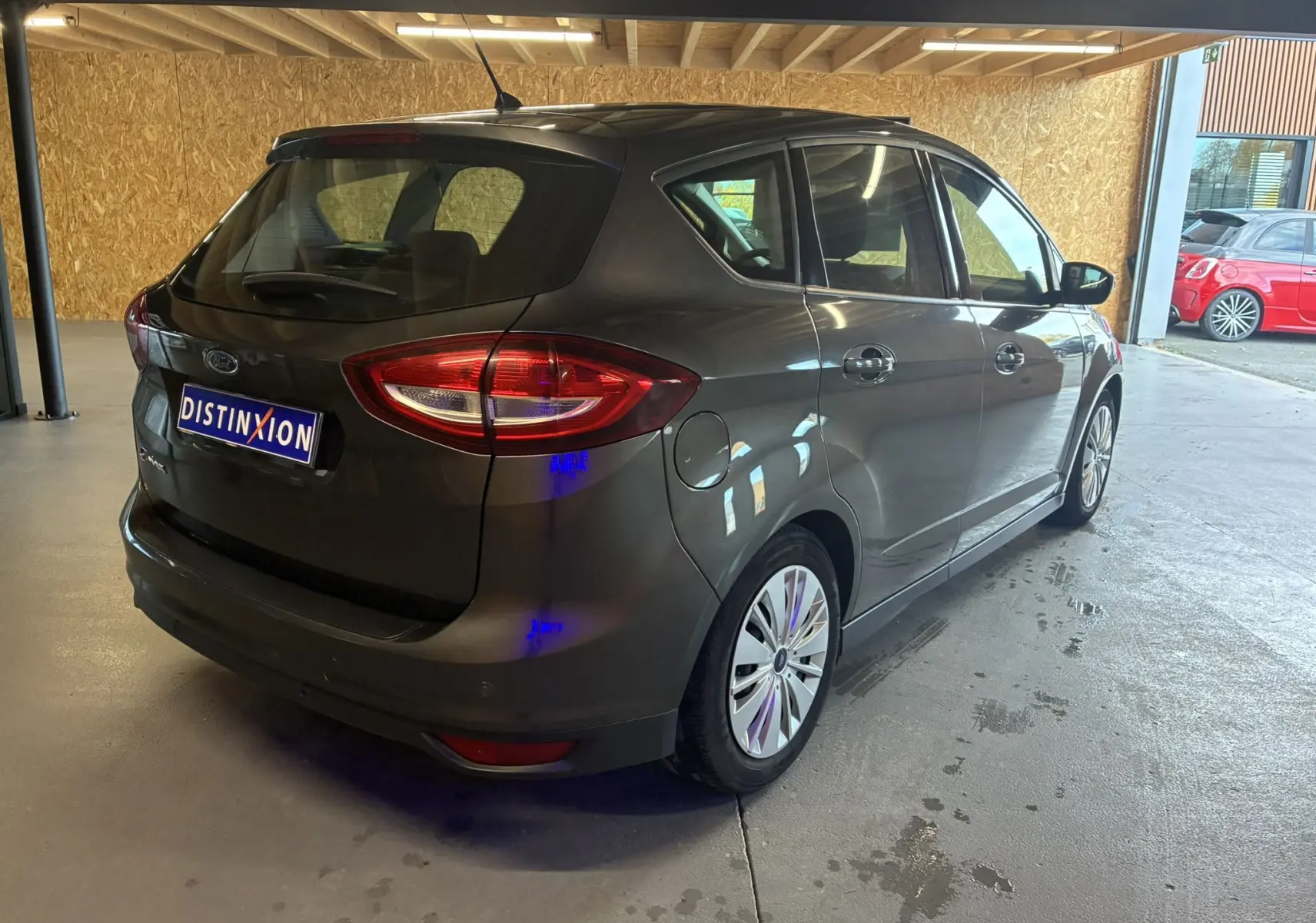 Vue 3/4 arrière droite d'une Ford C-MAX gris foncé 2015, avec hayon et feux arrière allongés dans un garage.