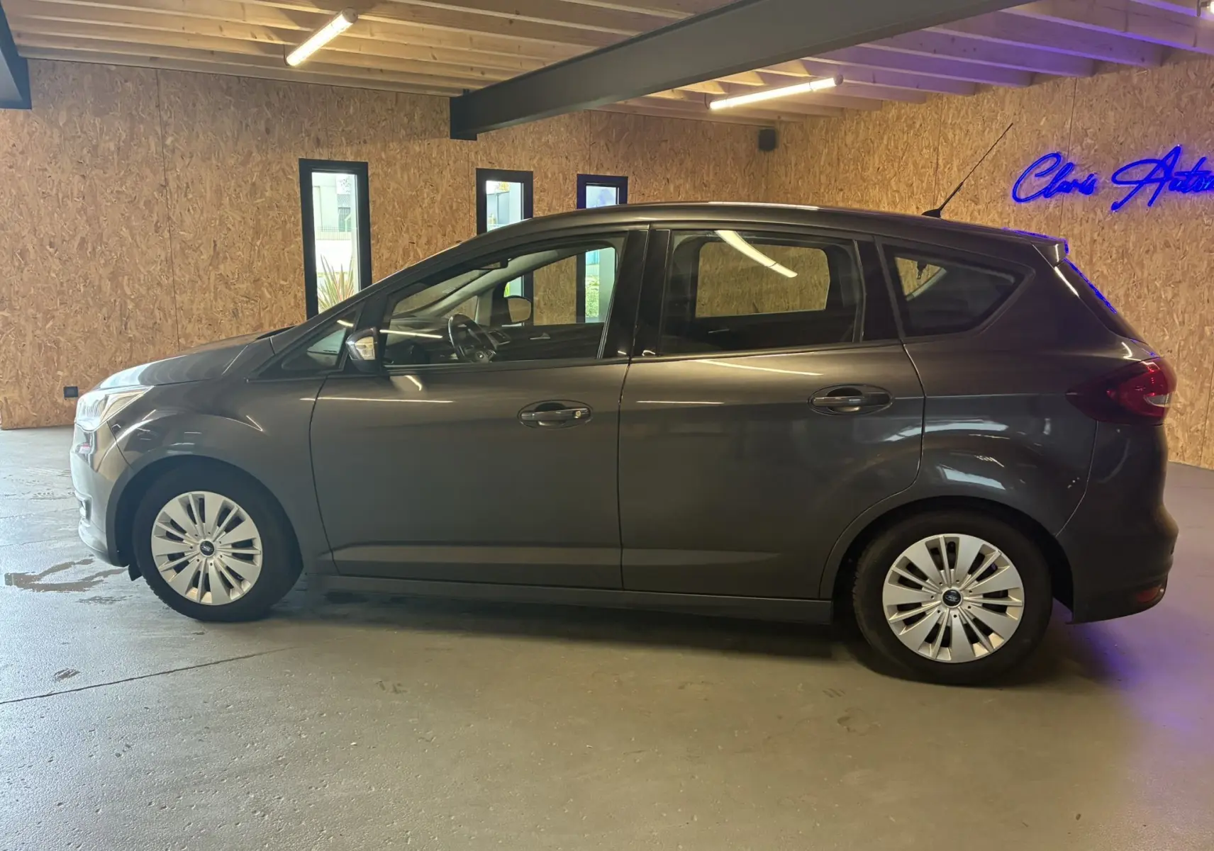Vue de profil côté gauche d'une Ford C-MAX gris métallisé garée en intérieur avec jantes argentées et vitres teintées.