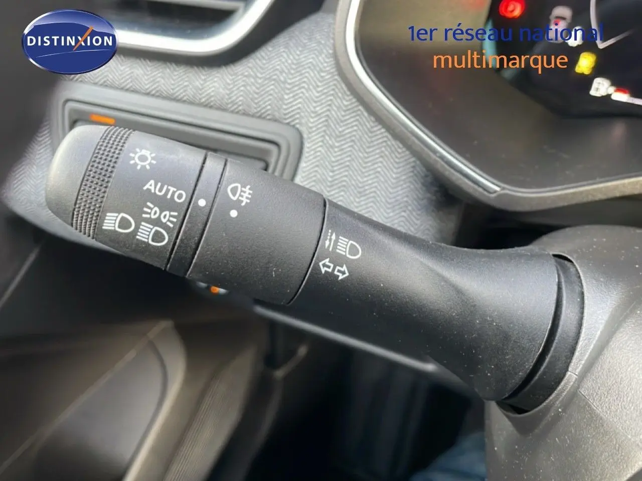 Gros plan sur la commande des feux et clignotants noire dans l’habitacle d’une Renault Clio rouge Désir Métal.