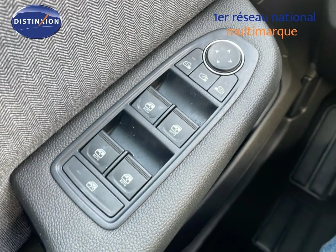 Gros plan sur les commandes des vitres électriques côté conducteur d’une Renault Clio 2025, tissu gris et plastique noir.