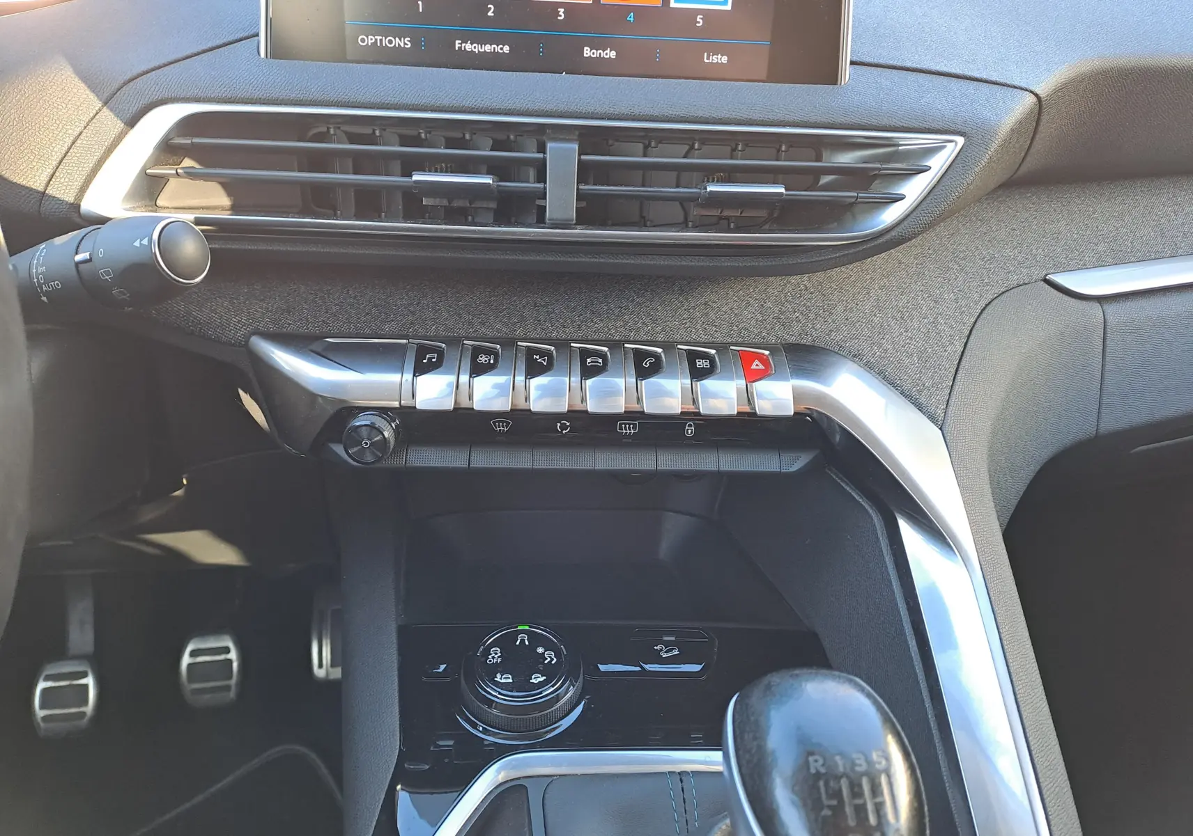 Vue intérieure centrée sur la console centrale et levier de vitesse manuelle d’un Peugeot 5008 gris, avec commandes et écran tactile visibles.