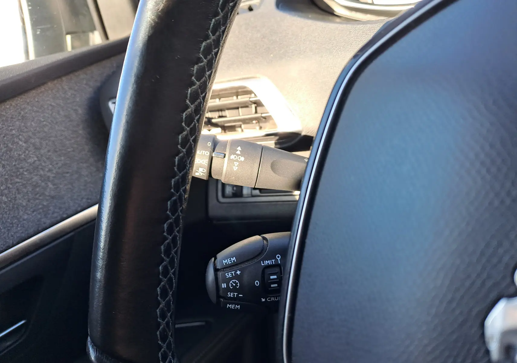 Gros plan sur le volant noir et les commandes de régulateur de vitesse du Peugeot 5008 gris, intérieur côté conducteur.