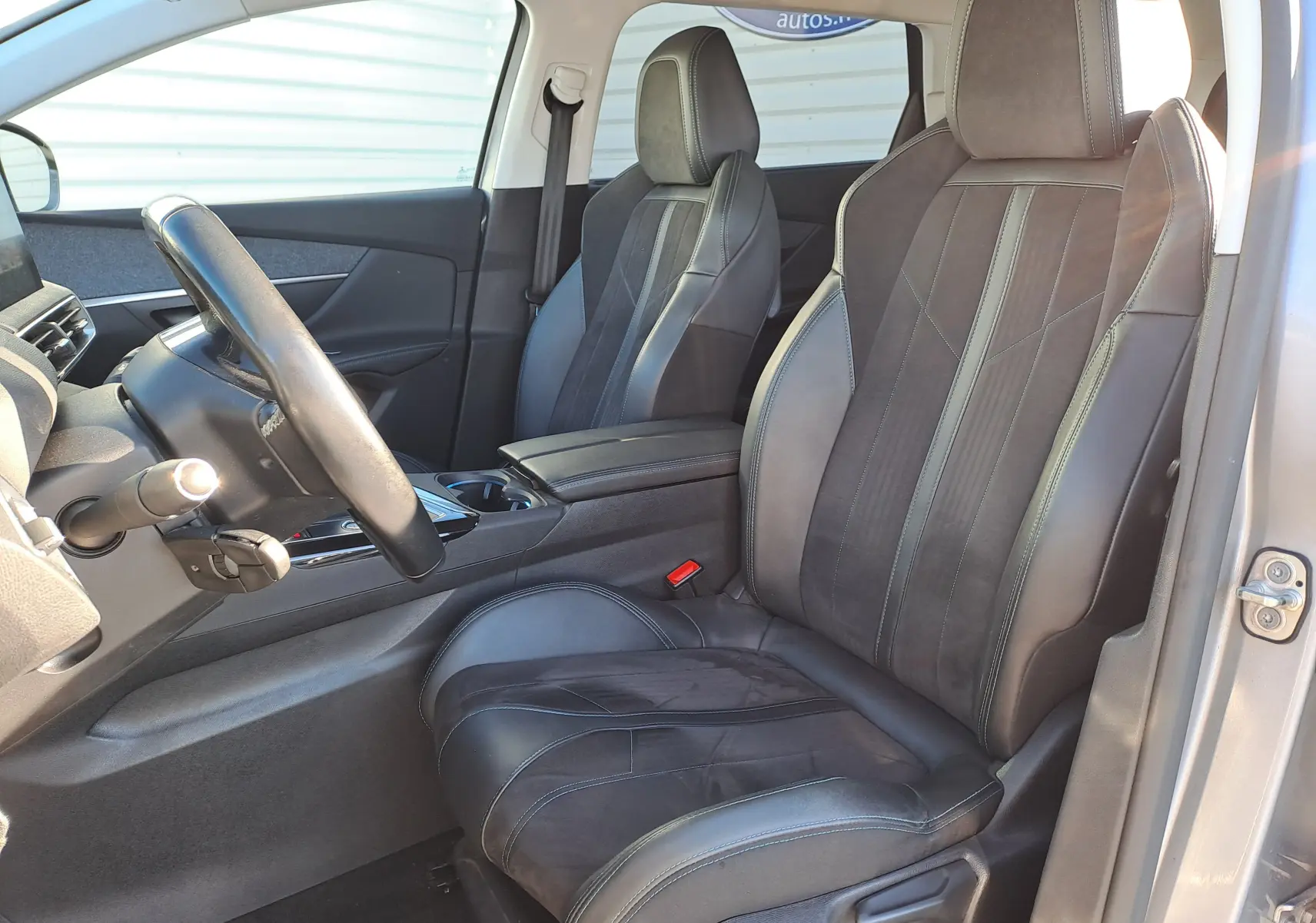 Vue intérieure côté conducteur du Peugeot 5008 gris, mettant en valeur les sièges en cuir et alcantara avec surpiqûres contrastées.