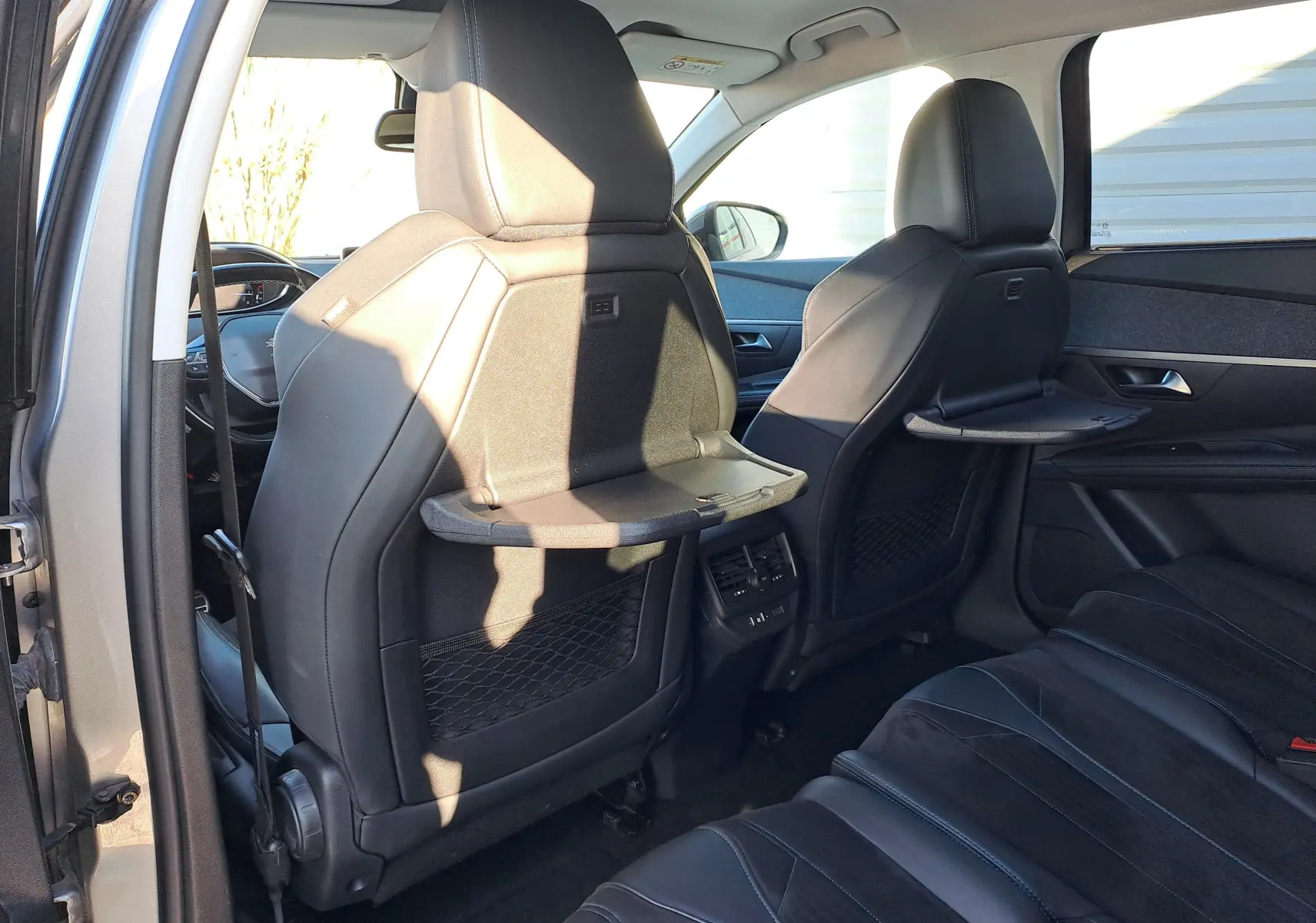 Vue intérieure arrière droite du Peugeot 5008 gris, montrant les sièges en cuir avec tablettes rabattables intégrées aux dossiers avant.