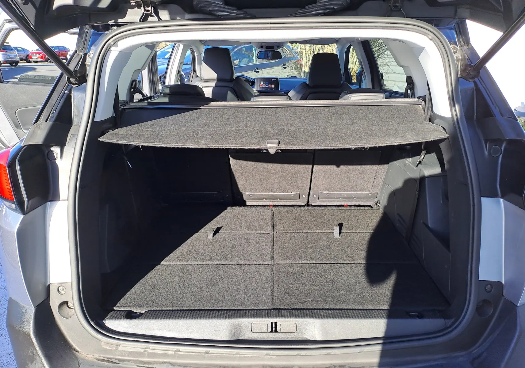 Vue arrière ouverte du coffre spacieux d’un Peugeot 5008 gris 2019 avec cache-bagages et sièges arrière visibles.