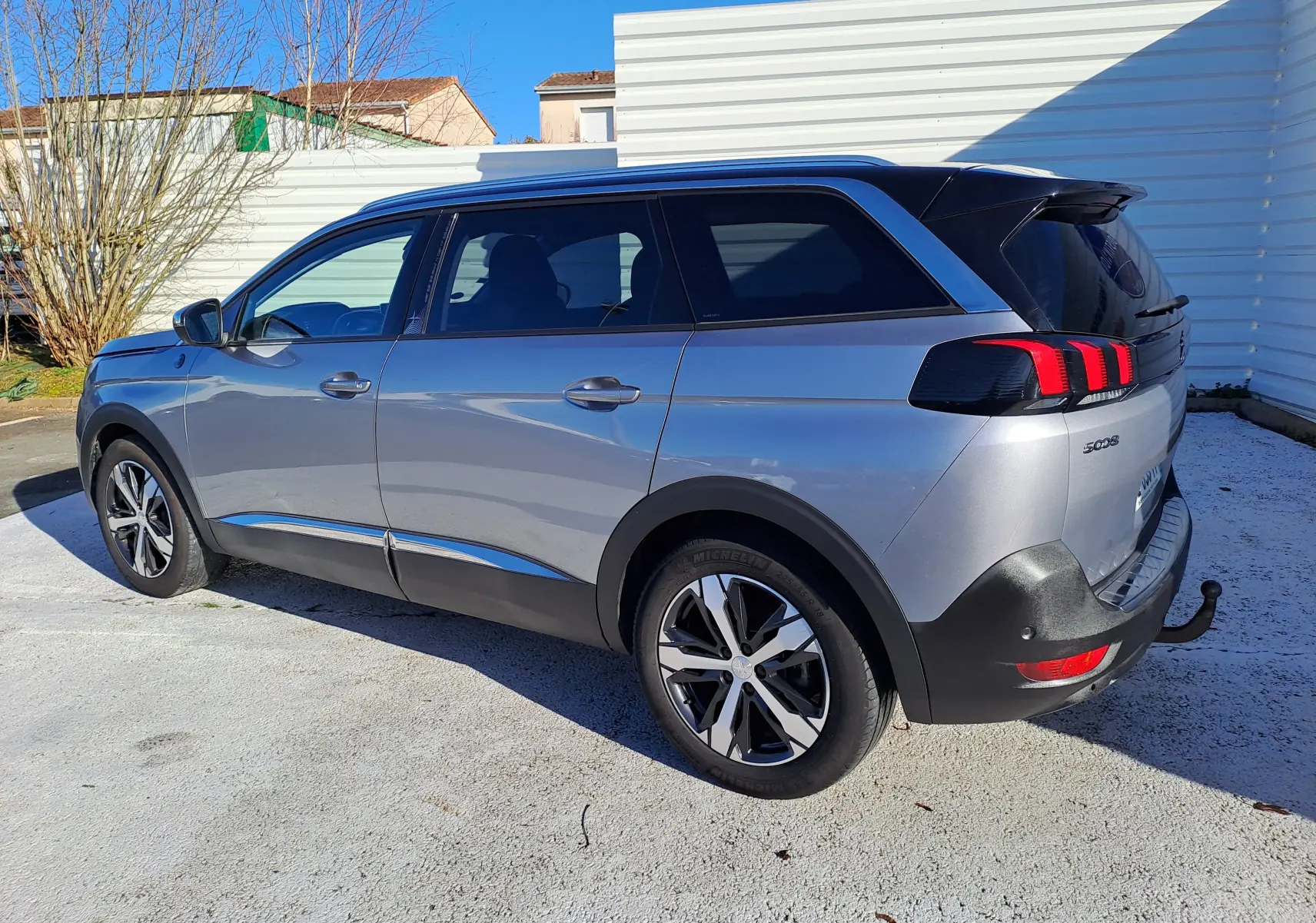 Peugeot 5008 gris vue 3/4 arrière droit, SUV 7 places avec feux arrière à griffes rouges et attelage visible.