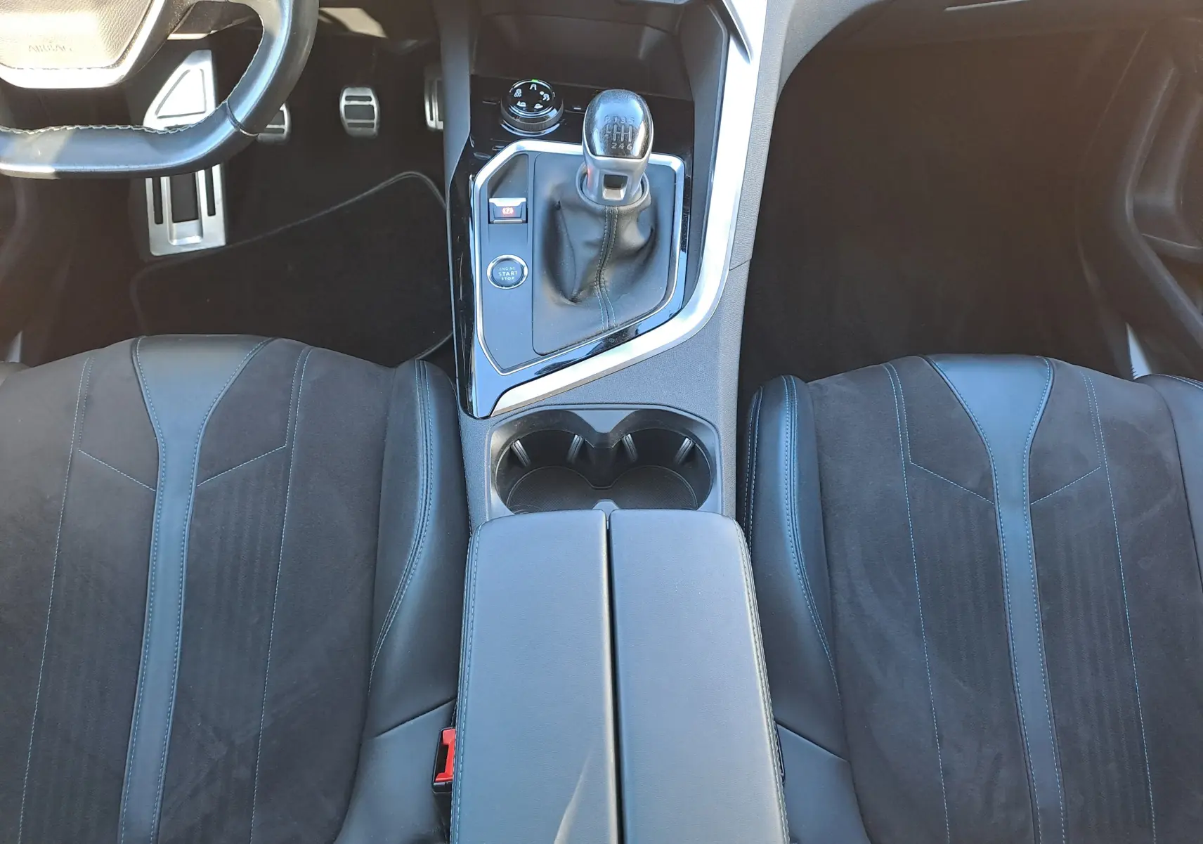 Vue intérieure centrée sur la console centrale et les sièges avant en cuir noir du Peugeot 5008 gris, boîte manuelle.