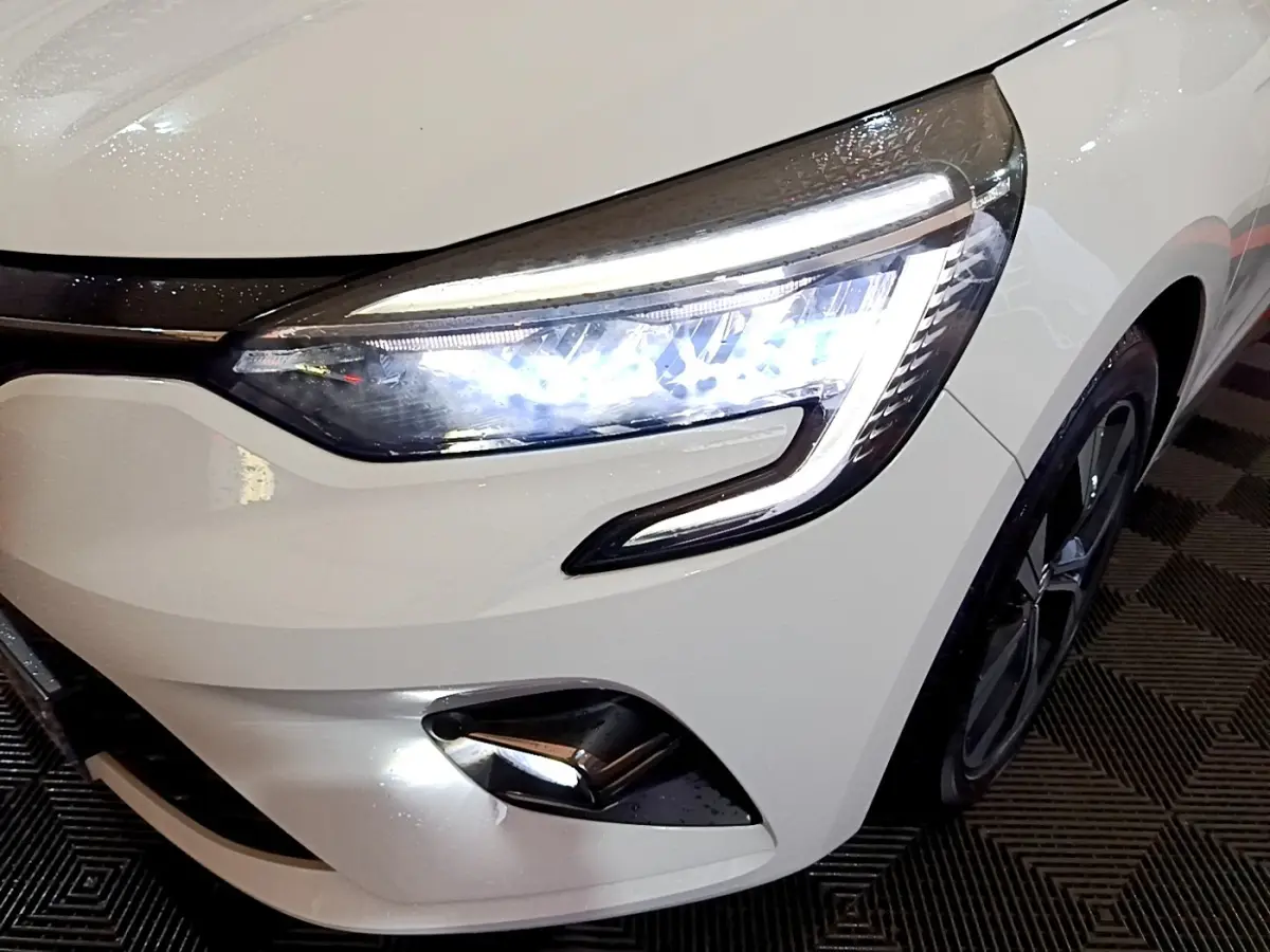 Gros plan sur l'avant droit blanc d'une Renault Clio 2023 avec phares LED allumés et jante noire visible.