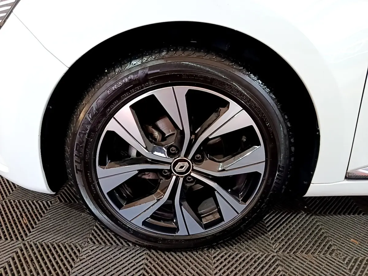 Gros plan sur la roue avant gauche d’une Renault Clio blanche avec jante alliage au design moderne bicolore.