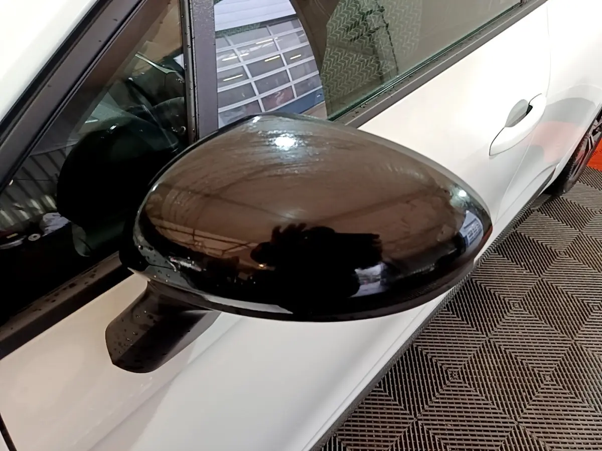 Rétroviseur noir en gros plan côté gauche sur Renault Clio Business blanc vue partielle du véhicule stationné.