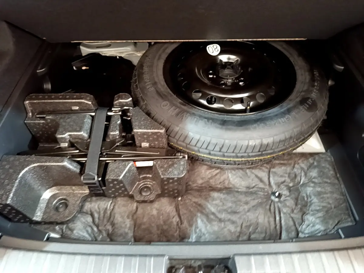 Vue du coffre ouvert du Renault Arkana blanc 2023, montrant la roue de secours et les outils de bord rangés.