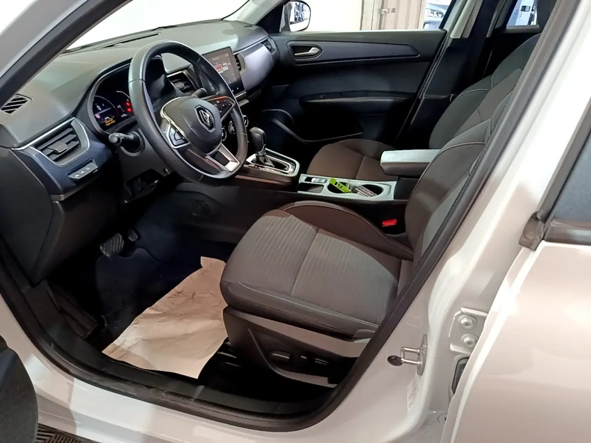 Vue intérieure côté conducteur d'une Renault Arkana blanc, montrant le volant cuir, tableau de bord et sièges tissu gris.